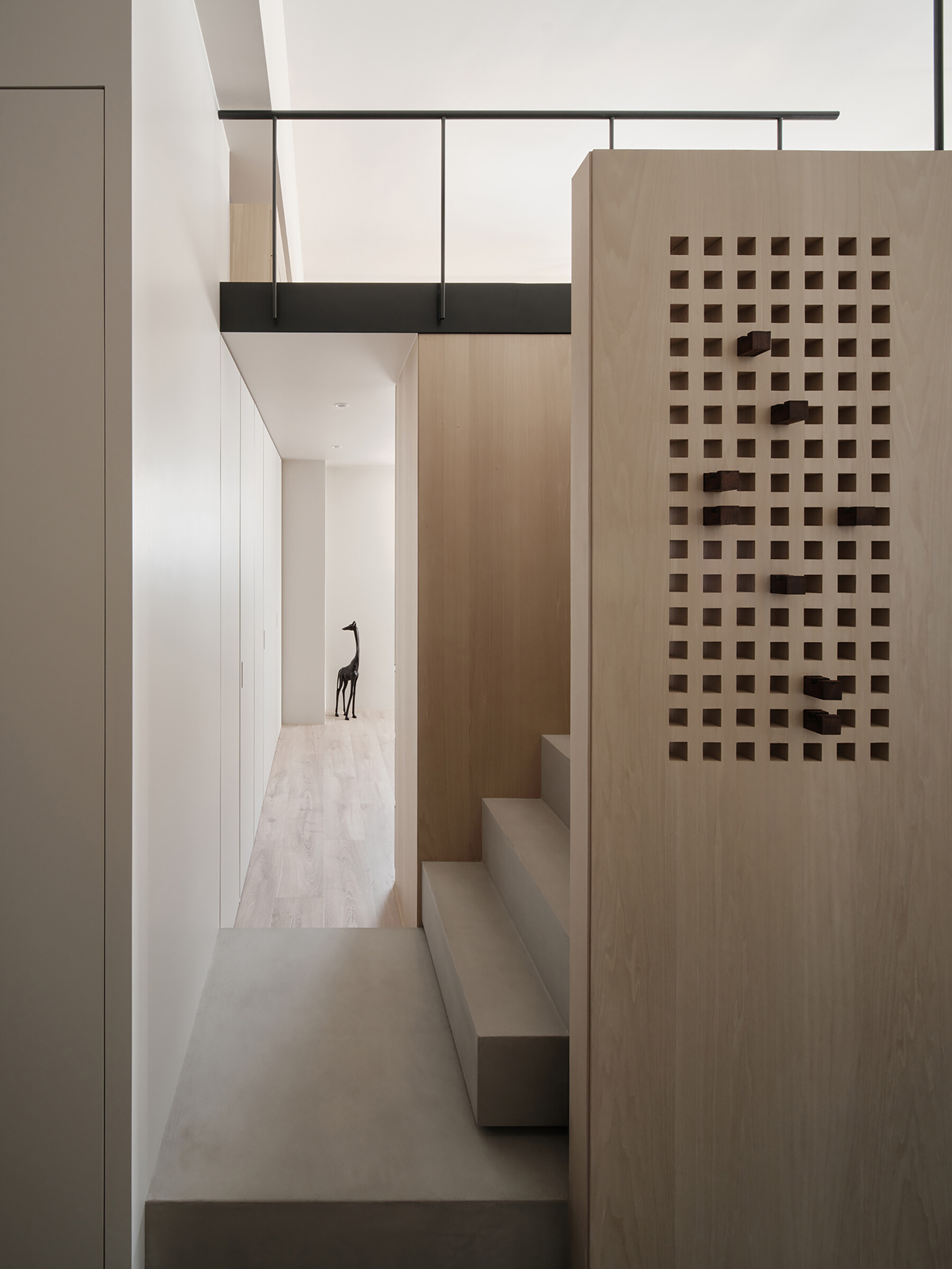 This staircase leading to the loft is more than just a means of access, it’s an architectural feature. Rather than feeling bulky, it reads as an extension of the home’s material language. Slim, pale wood treads and light metal framing keep the look airy, while maintaining stability and safety. The stair’s placement also supports the apartment’s “dual circulation” layout, ensuring clear, logical flow between living zones.