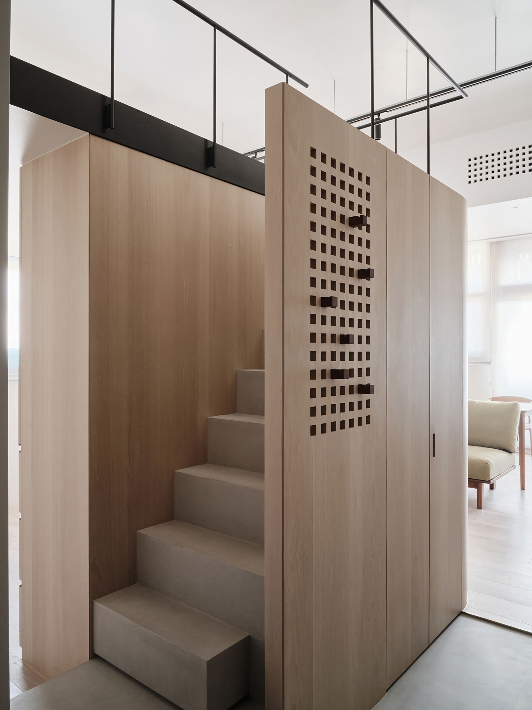 This staircase leading to the loft is more than just a means of access, it’s an architectural feature. Rather than feeling bulky, it reads as an extension of the home’s material language. Slim, pale wood treads and light metal framing keep the look airy, while maintaining stability and safety. The stair’s placement also supports the apartment’s “dual circulation” layout, ensuring clear, logical flow between living zones.