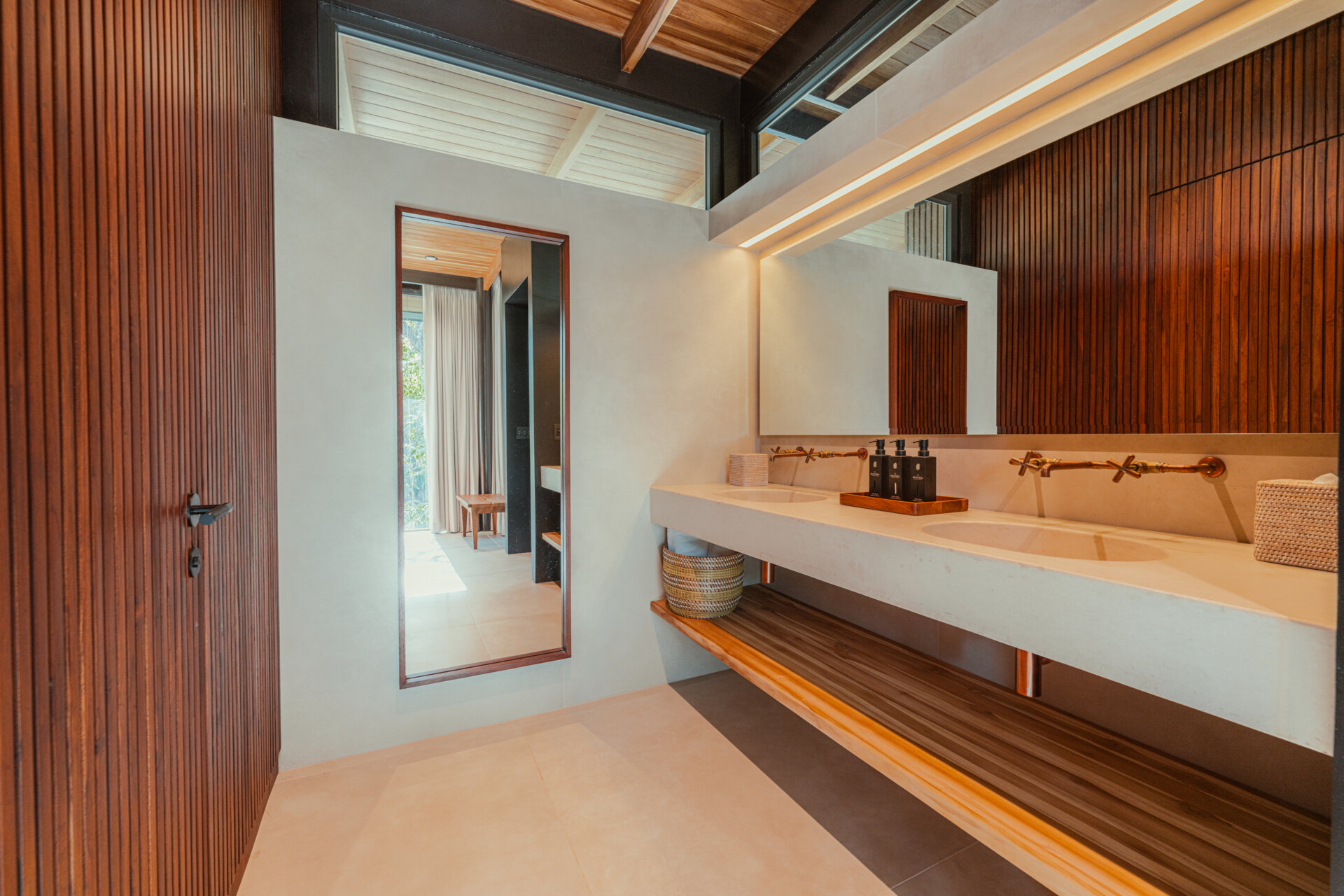 This serene bathroom pairs a floating concrete vanity with warm brass fixtures for a modern, spa-like feel. Vertical wood paneling adds natural texture, while soft daylight and clean lines create a calm, grounded atmosphere.