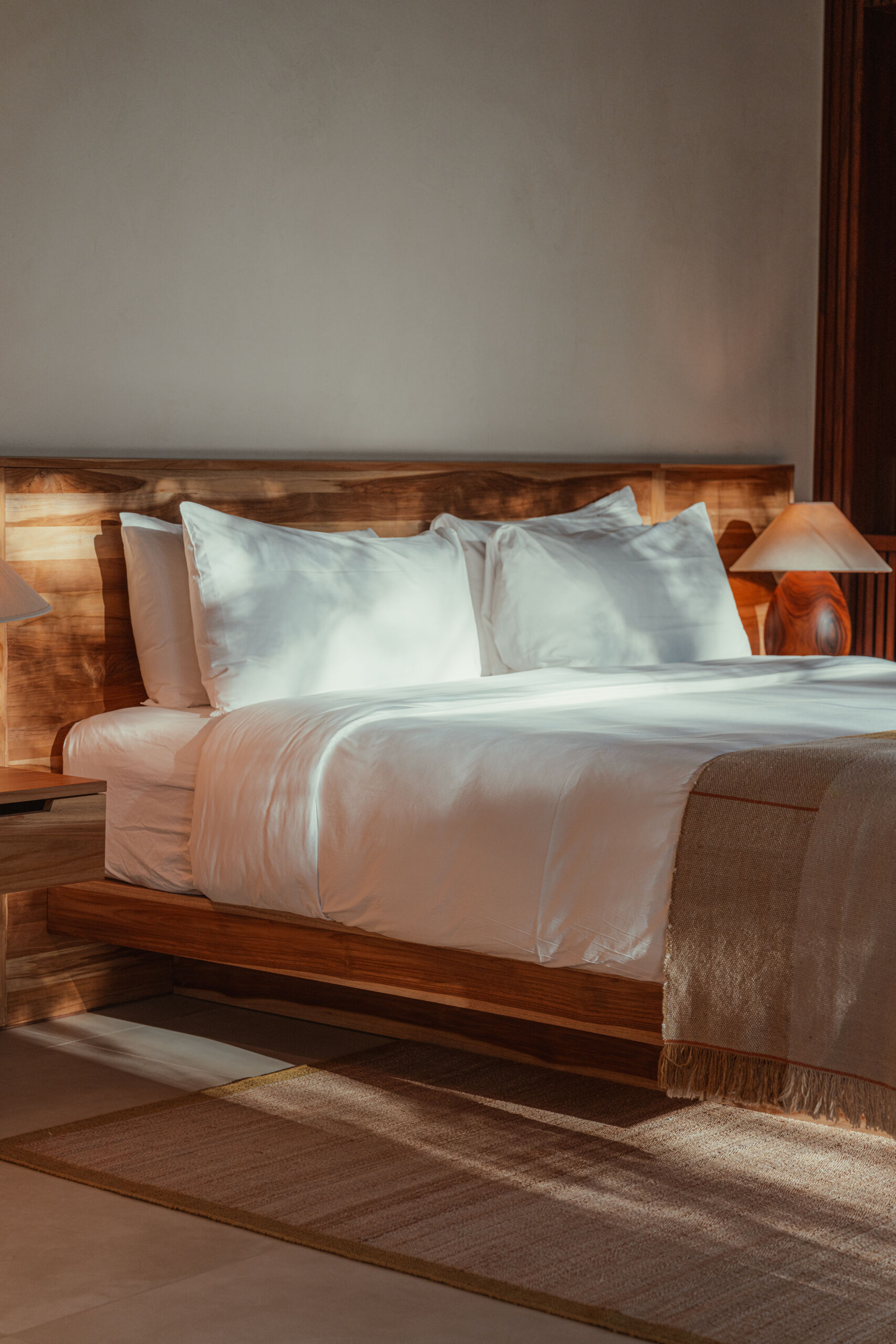 This warm, light-filled guest accommodation invites rest and relaxation. Sheer curtains, natural wood paneling and ceiling, and sculpted side tables create a calm, handcrafted feel, while the low bed and open layout make space for slow, restful moments.
