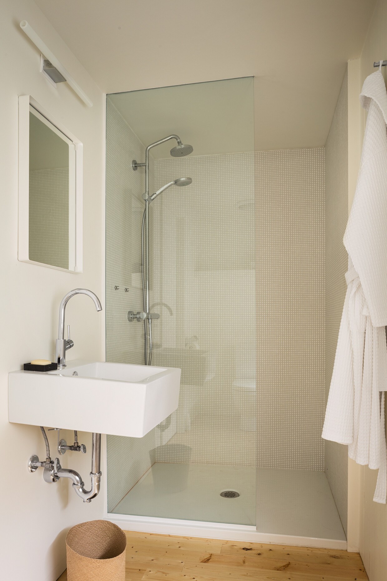 A minimalist bathroom with mosaic tile, soft light, and clean lines. A wall-mounted sink and simple touches like a woven basket add quiet charm.