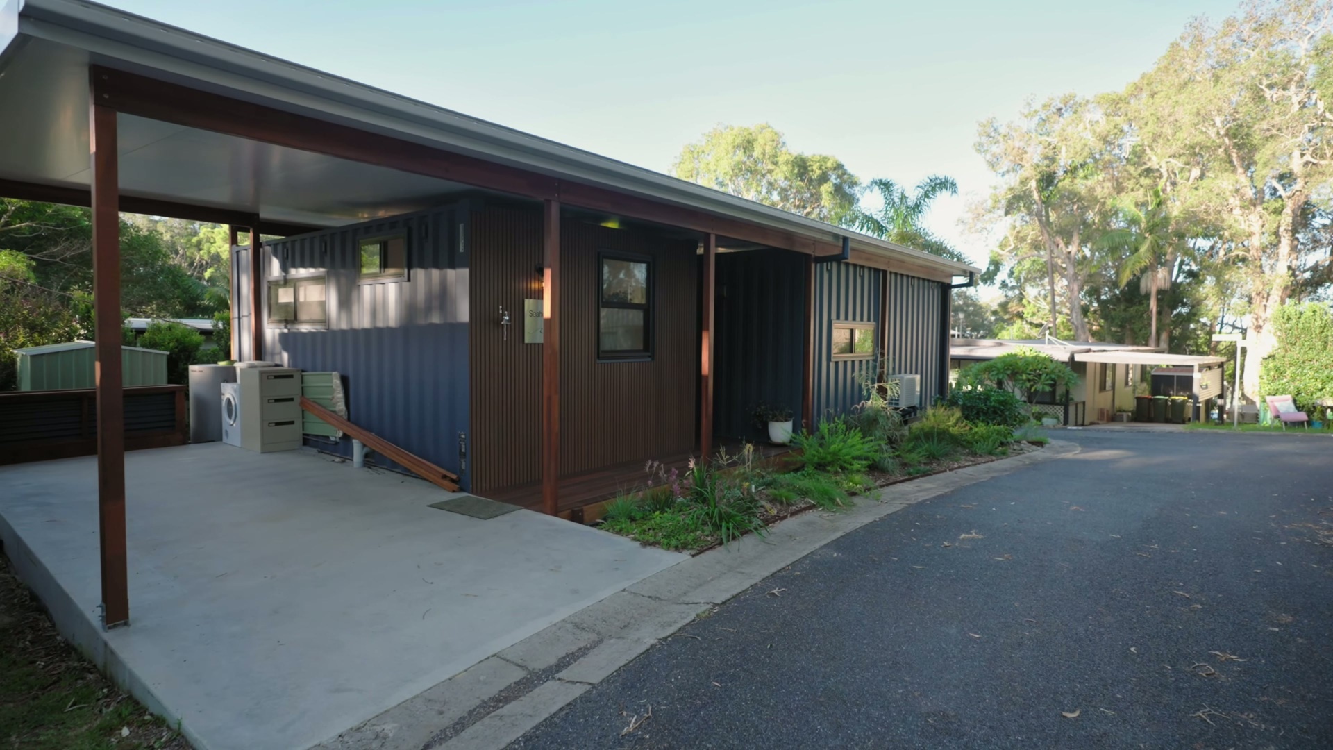 A compact modular home with warm timber-look cladding, custom awnings, and a simple coastal palette that blends into its leafy Sawtell surroundings.