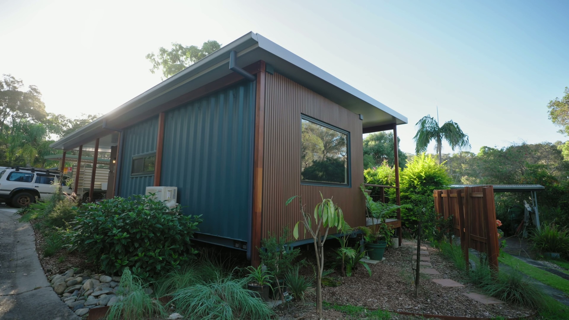 A compact modular home with warm timber-look cladding, custom awnings, and a simple coastal palette that blends into its leafy Sawtell surroundings.