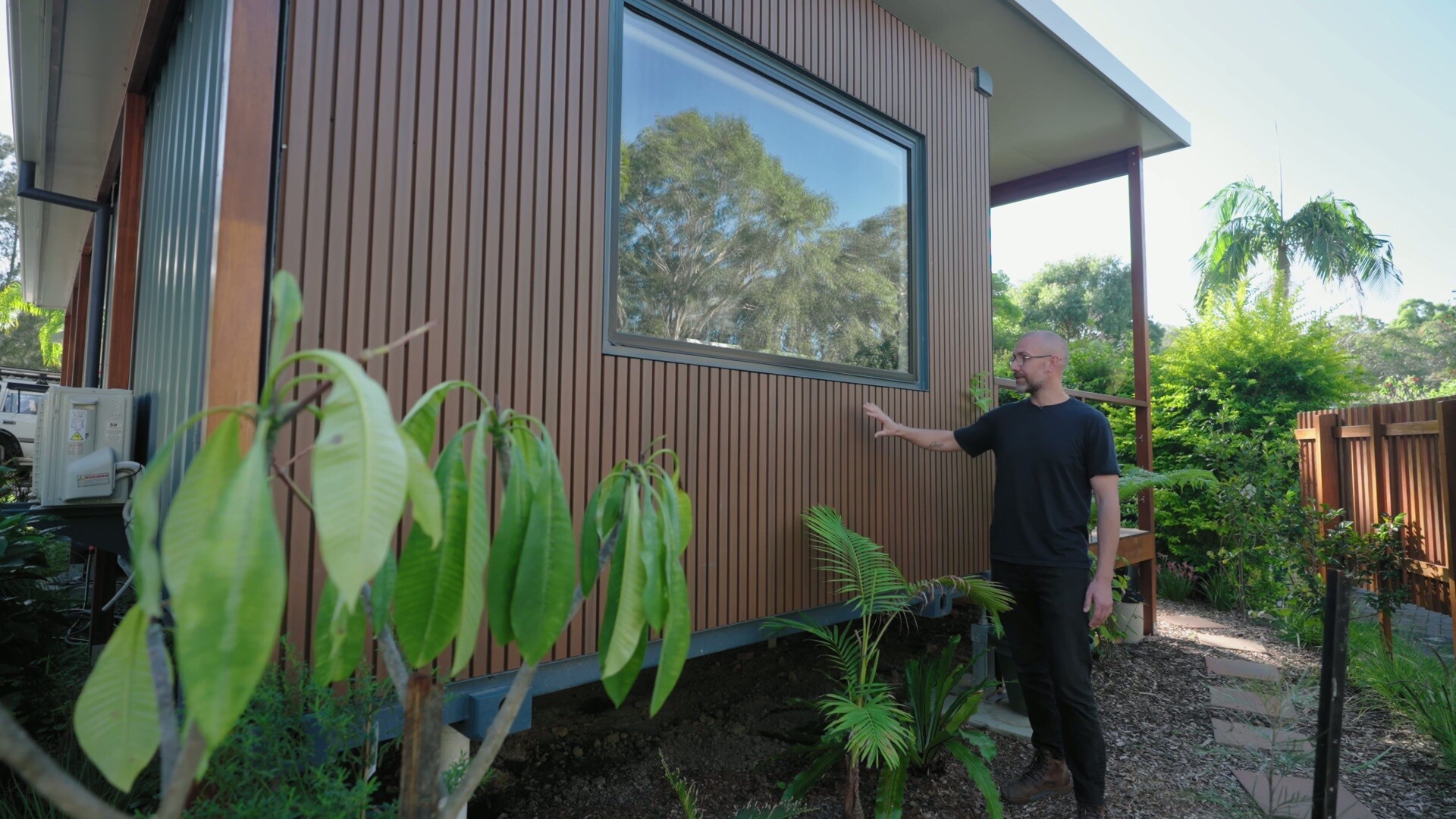 A compact modular home with warm timber-look cladding, custom awnings, and a simple coastal palette that blends into its leafy Sawtell surroundings.