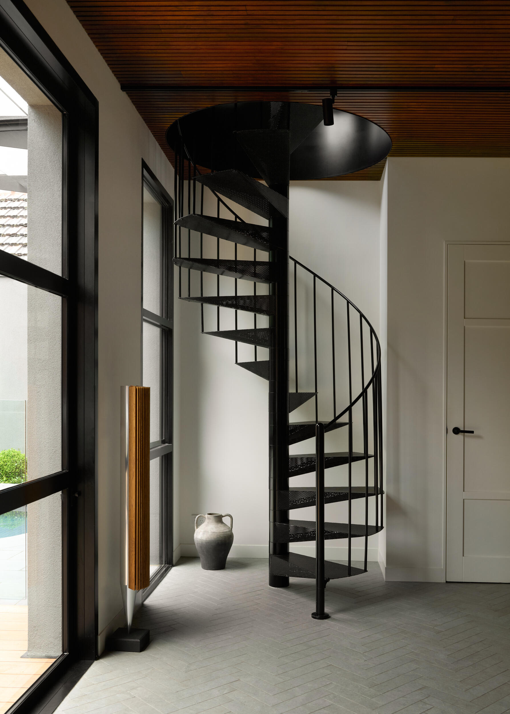 This secondary spiral staircase feels like a piece of modern sculpture quietly tucked into the corner. Made from black metal, its form is both bold and airy, casting soft shadows that shift throughout the day. The wood-lined ceiling above warms the room and the horizontal lines contrast beautifully with the stair’s vertical ascent.
