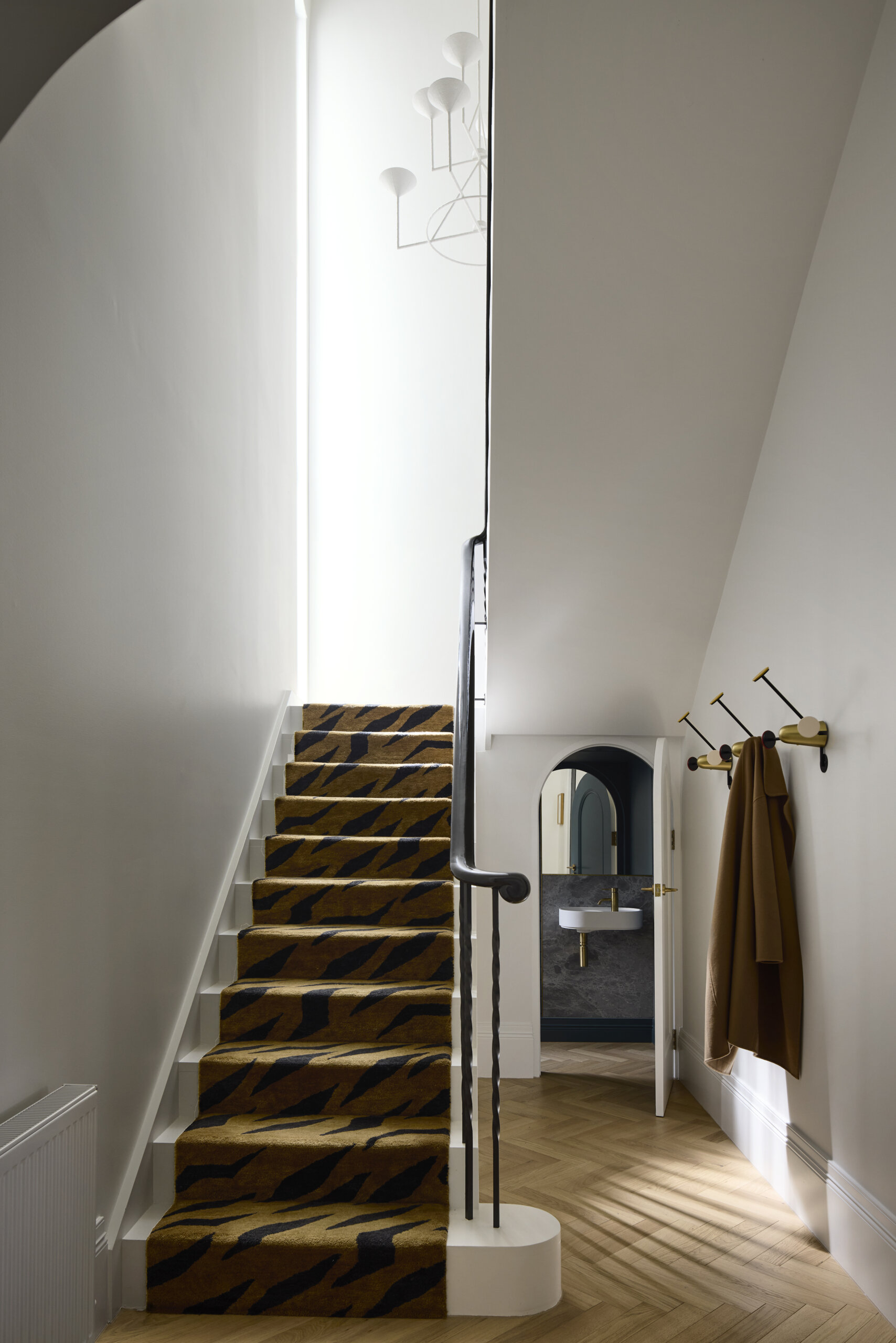 This stairwell is quietly expressive, defined by a patterned runner that brings a sense of movement to the otherwise pared-back architecture. Overhead, a sculptural pendant lends just enough presence, adding to the space’s sense of rhythm and quiet intent.