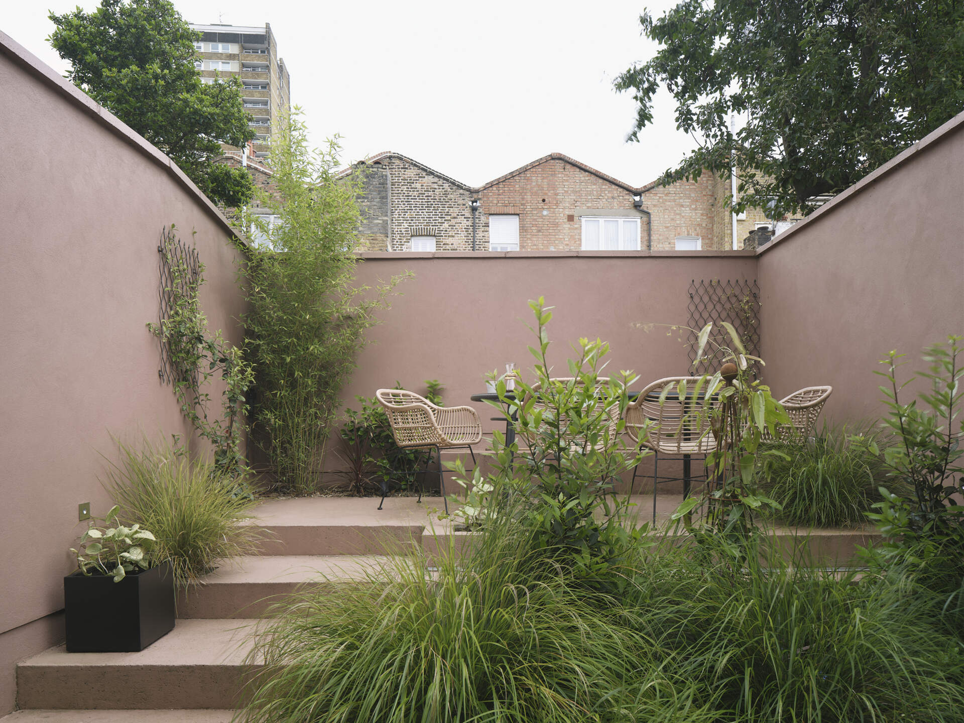 This terrace garden becomes the focal point of the home, with a series of steps and built-in planters guiding users to the top, where a private elevated space features a table and chairs, offering a quiet spot to relax or entertain, surrounded by walls and greenery. This layered outdoor area continues the home’s theme of connected, purposeful spaces.
