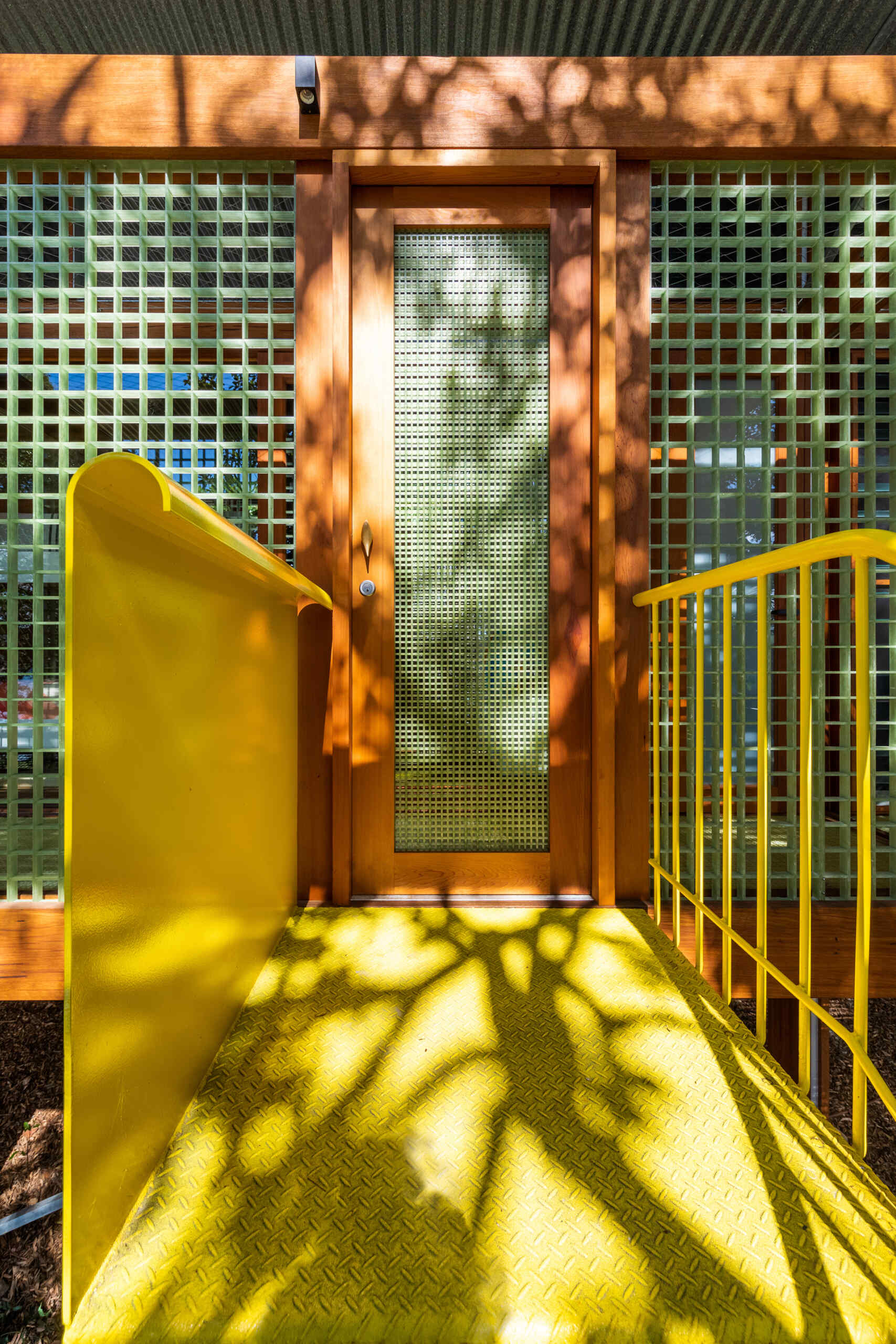 A bold yellow spiral staircase winds up through the stone and foliage, adding a playful sculptural twist to this quiet treetop home.
