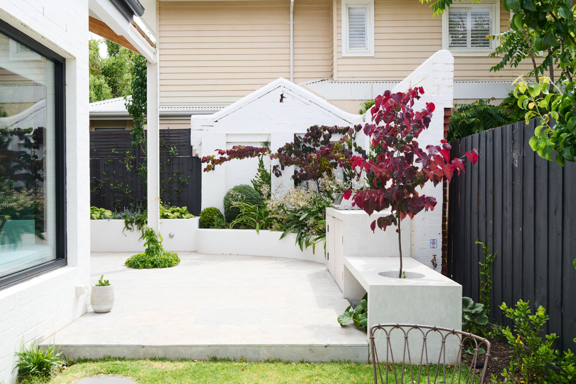 This tranquil alfresco area transforms a former garage wall into a cozy garden retreat. Layered planting, a timber pergola, and a built-in BBQ make it perfect for relaxing or entertaining outdoors.