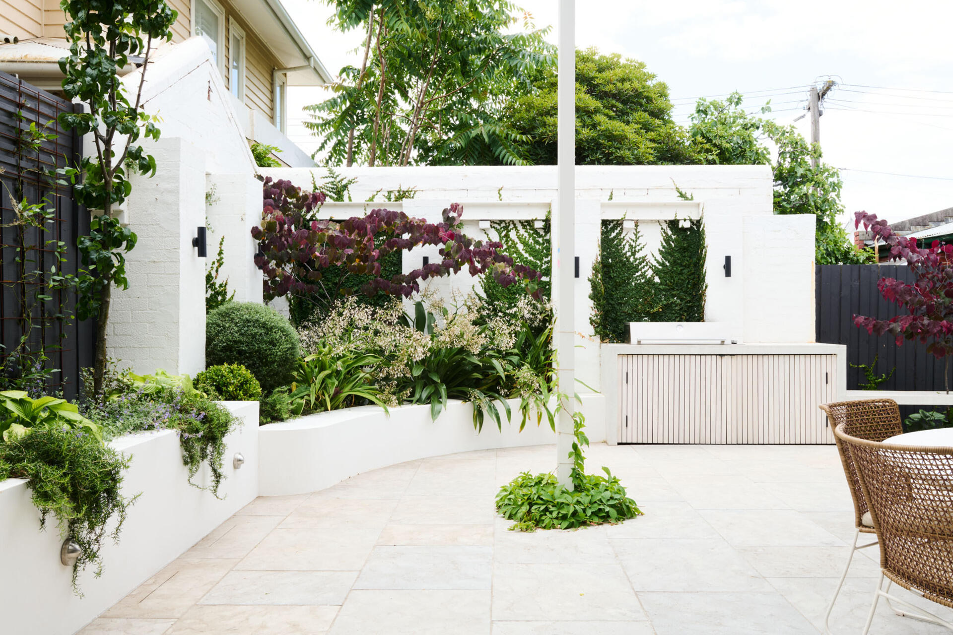 This tranquil alfresco area transforms a former garage wall into a cozy garden retreat. Layered planting, a timber pergola, and a built-in BBQ make it perfect for relaxing or entertaining outdoors.