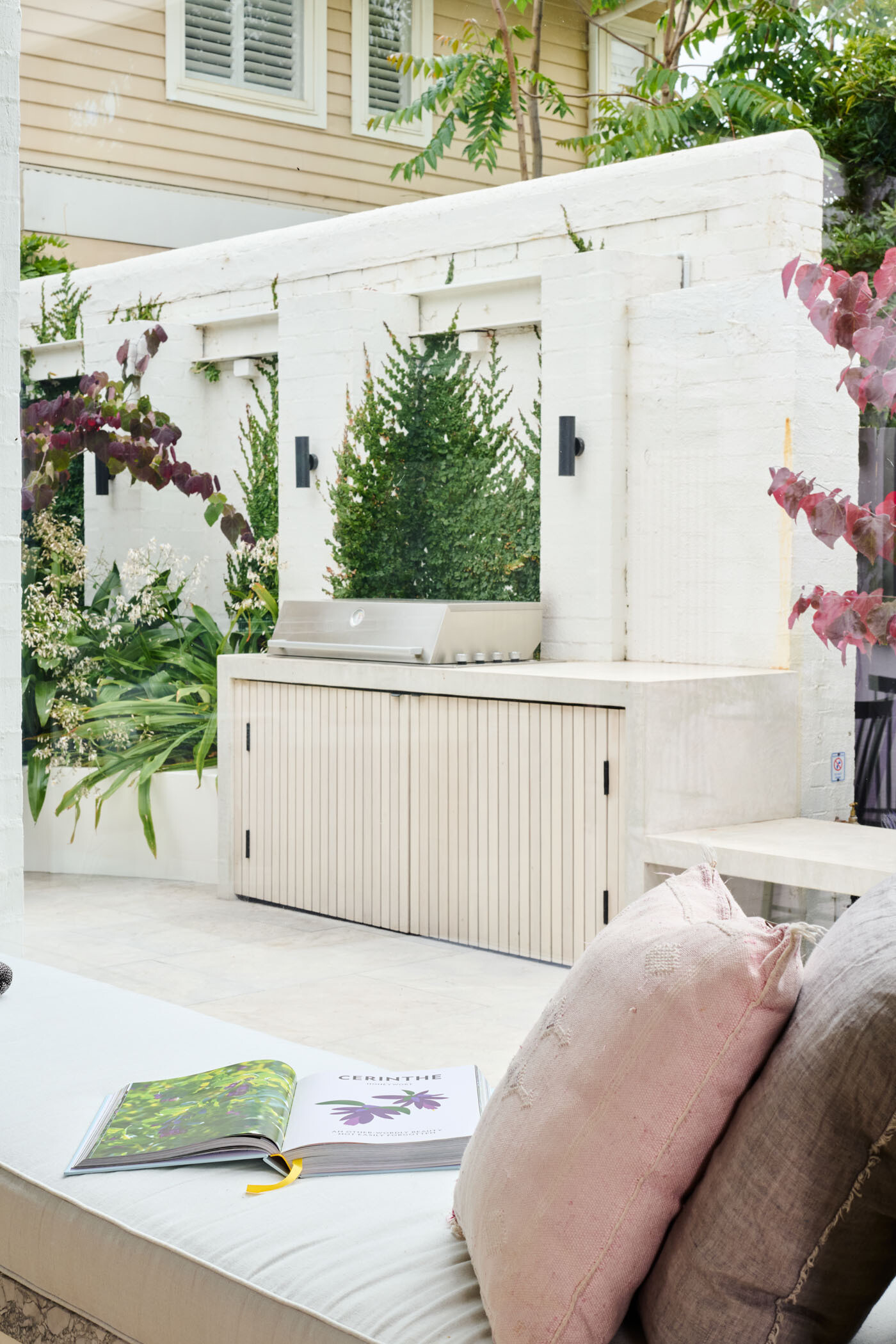 This tranquil alfresco area transforms a former garage wall into a cozy garden retreat. Layered planting, a timber pergola, and a built-in BBQ make it perfect for relaxing or entertaining outdoors.