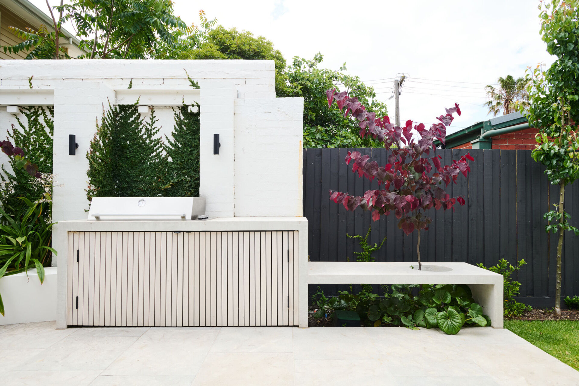 This tranquil alfresco area transforms a former garage wall into a cozy garden retreat. Layered planting, a timber pergola, and a built-in BBQ make it perfect for relaxing or entertaining outdoors.