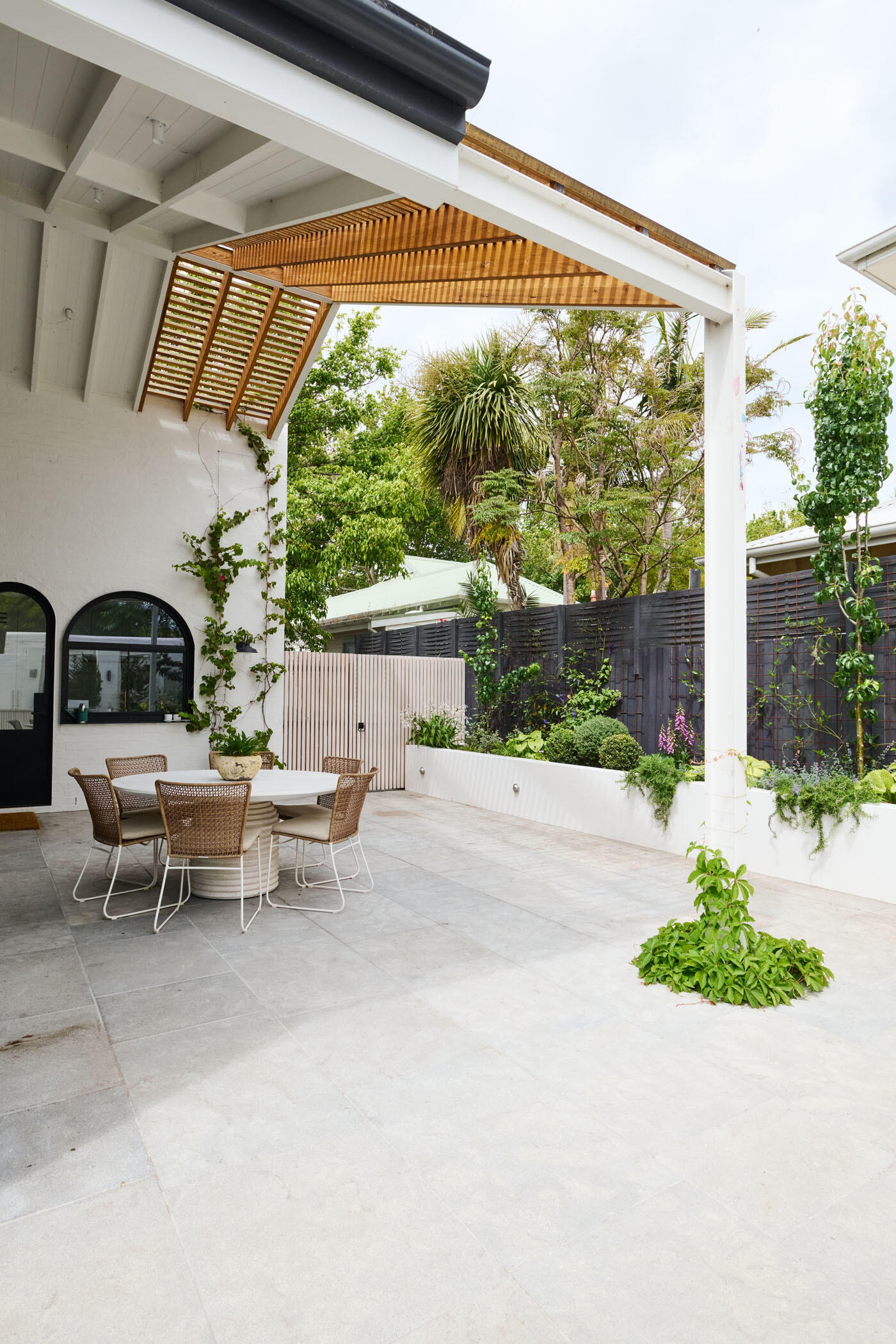 This tranquil alfresco area transforms a former garage wall into a cozy garden retreat. Layered planting, a timber pergola, and a built-in BBQ make it perfect for relaxing or entertaining outdoors.