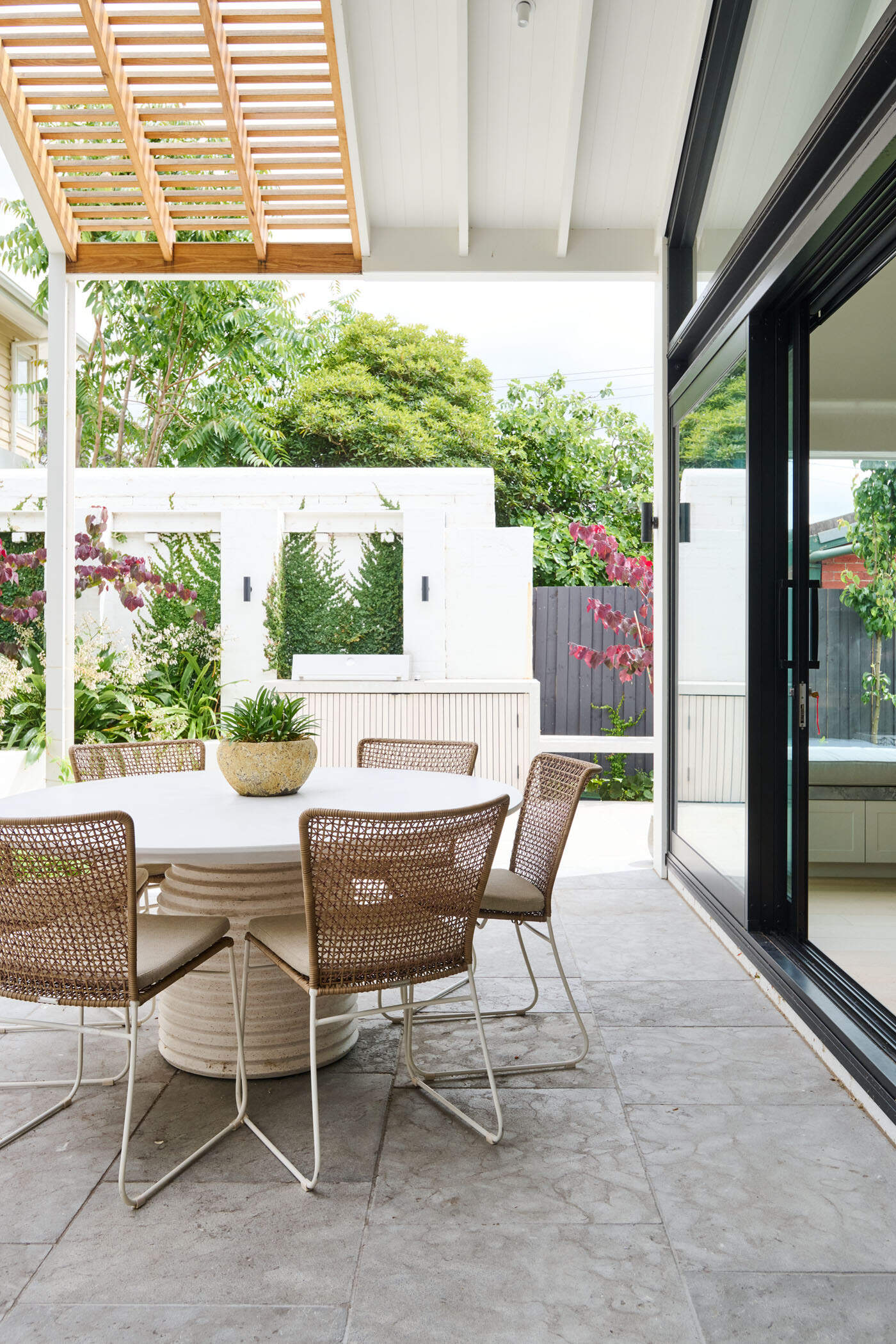 This tranquil alfresco area transforms a former garage wall into a cozy garden retreat. Layered planting, a timber pergola, and a built-in BBQ make it perfect for relaxing or entertaining outdoors.