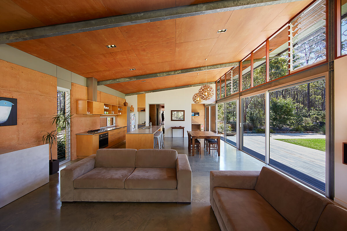 Timber-lined ceilings, a rammed earth wall, and natural materials create a warm, open interior that feels both grounded and connected to the bush.