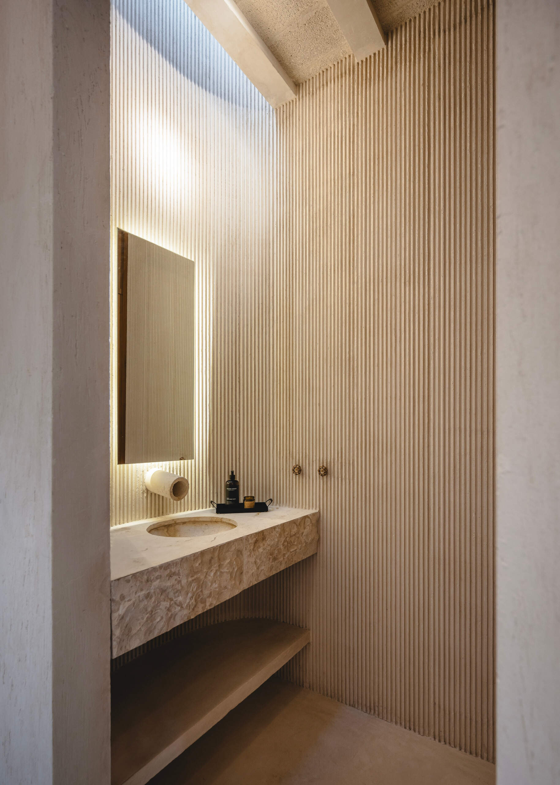 Bathrooms throughout the home are defined by tactile materials and natural light. Crescent-shaped skylights frame the open sky above, casting shifting patterns onto lime-plastered walls and hand-finished concrete surfaces. The design is restrained yet expressive, using local techniques to create spaces that feel at once grounded and ethereal.