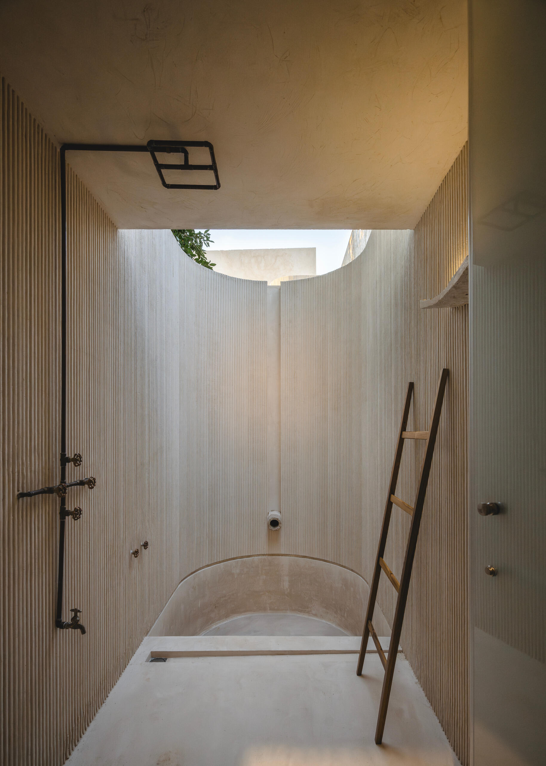 Bathrooms throughout the home are defined by tactile materials and natural light. Crescent-shaped skylights frame the open sky above, casting shifting patterns onto lime-plastered walls and hand-finished concrete surfaces. The design is restrained yet expressive, using local techniques to create spaces that feel at once grounded and ethereal.