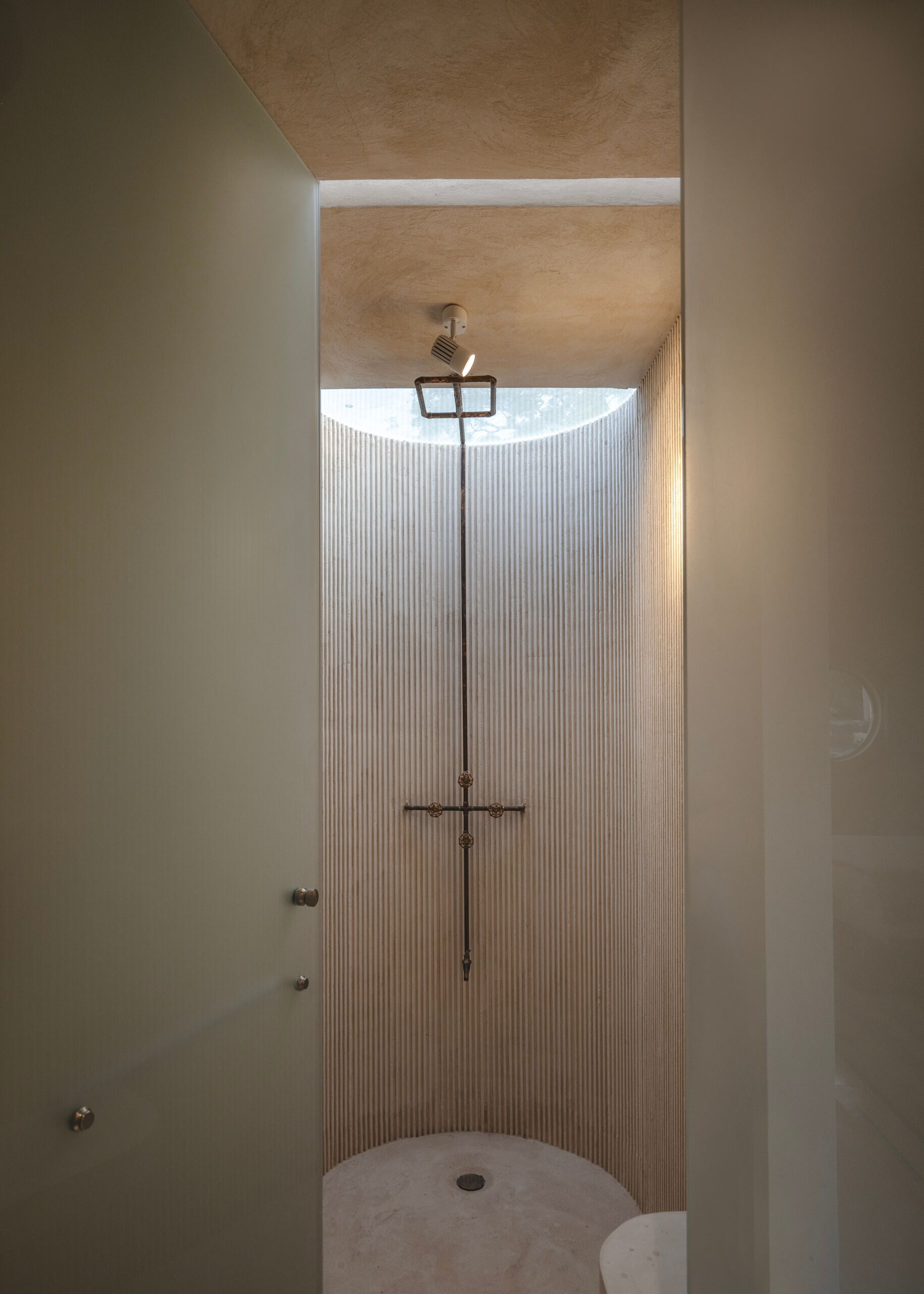 Bathrooms throughout the home are defined by tactile materials and natural light. Crescent-shaped skylights frame the open sky above, casting shifting patterns onto lime-plastered walls and hand-finished concrete surfaces. The design is restrained yet expressive, using local techniques to create spaces that feel at once grounded and ethereal.