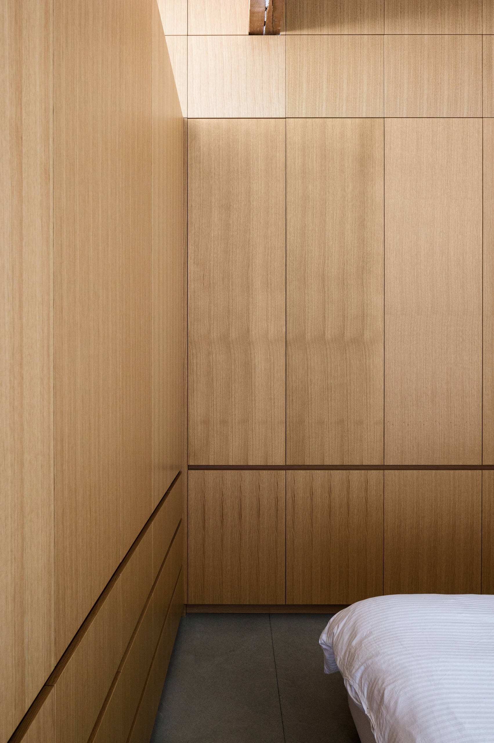 In this serene loft bedroom, custom cabinetry hides both essentials and surprises—including a wine collection. Modern comfort with a personal twist.