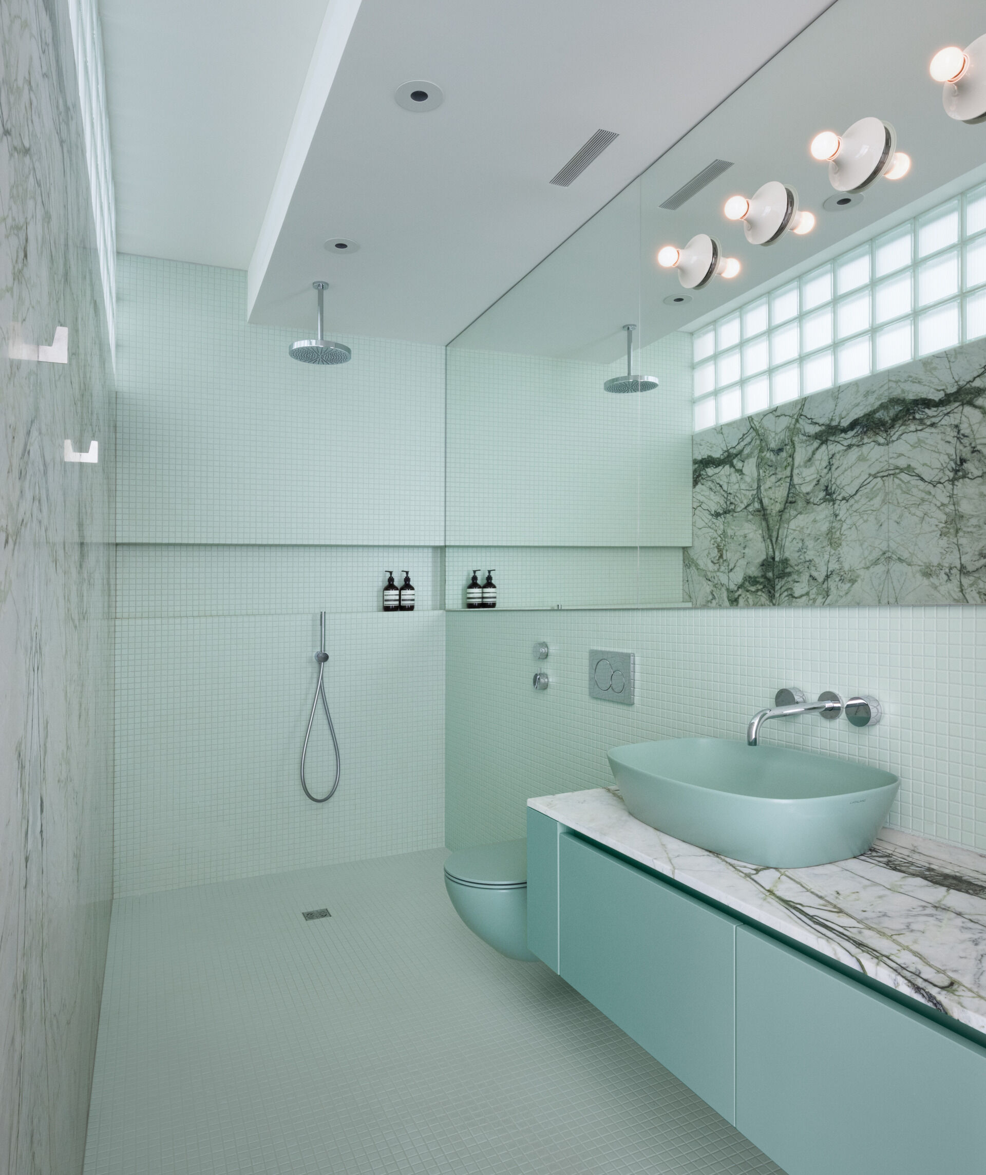 Calacatta verde marble, soft tile, and retro glass blocks bring luxury and light into this modern Montreal bathroom with timeless flair.