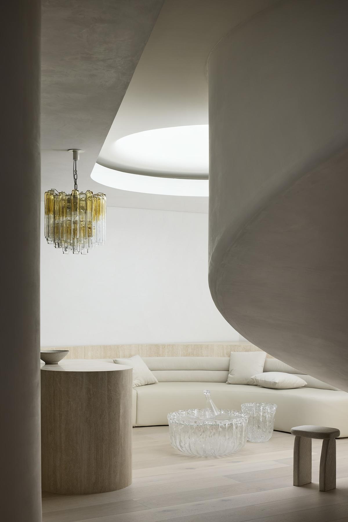 A lounge and bar area features curved built-in seating and soft overhead light, creating a moment of architectural intimacy. Rippled bronze glass doors and vintage French brass accents add a glamorous edge to the cocktail bar nearby.