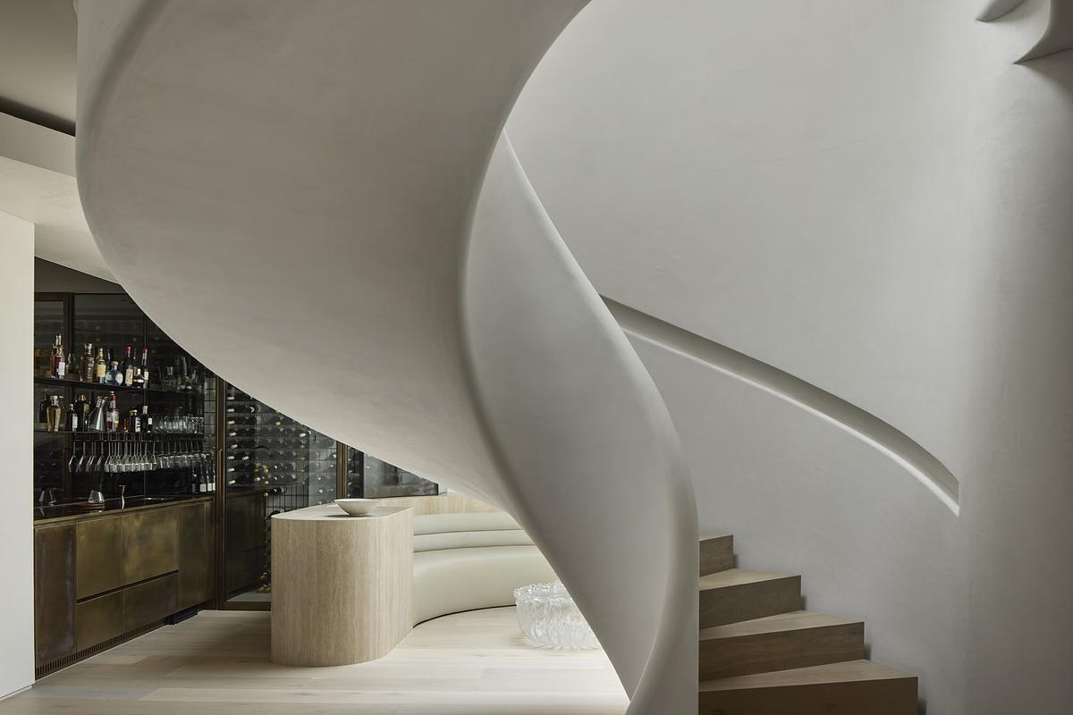 A lounge and bar area features curved built-in seating and soft overhead light, creating a moment of architectural intimacy. Rippled bronze glass doors and vintage French brass accents add a glamorous edge to the cocktail bar nearby.