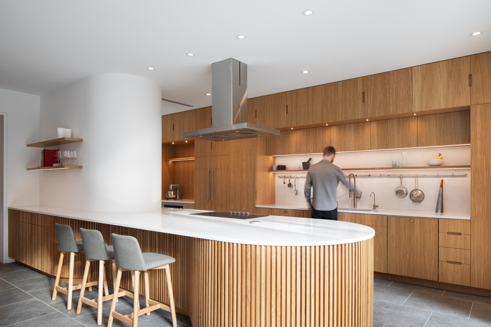 A sculptural oak island and seamless floor-to-ceiling cabinetry define this light-filled Montreal kitchen, where natural materials and soft curves create a warm, minimalist atmosphere.