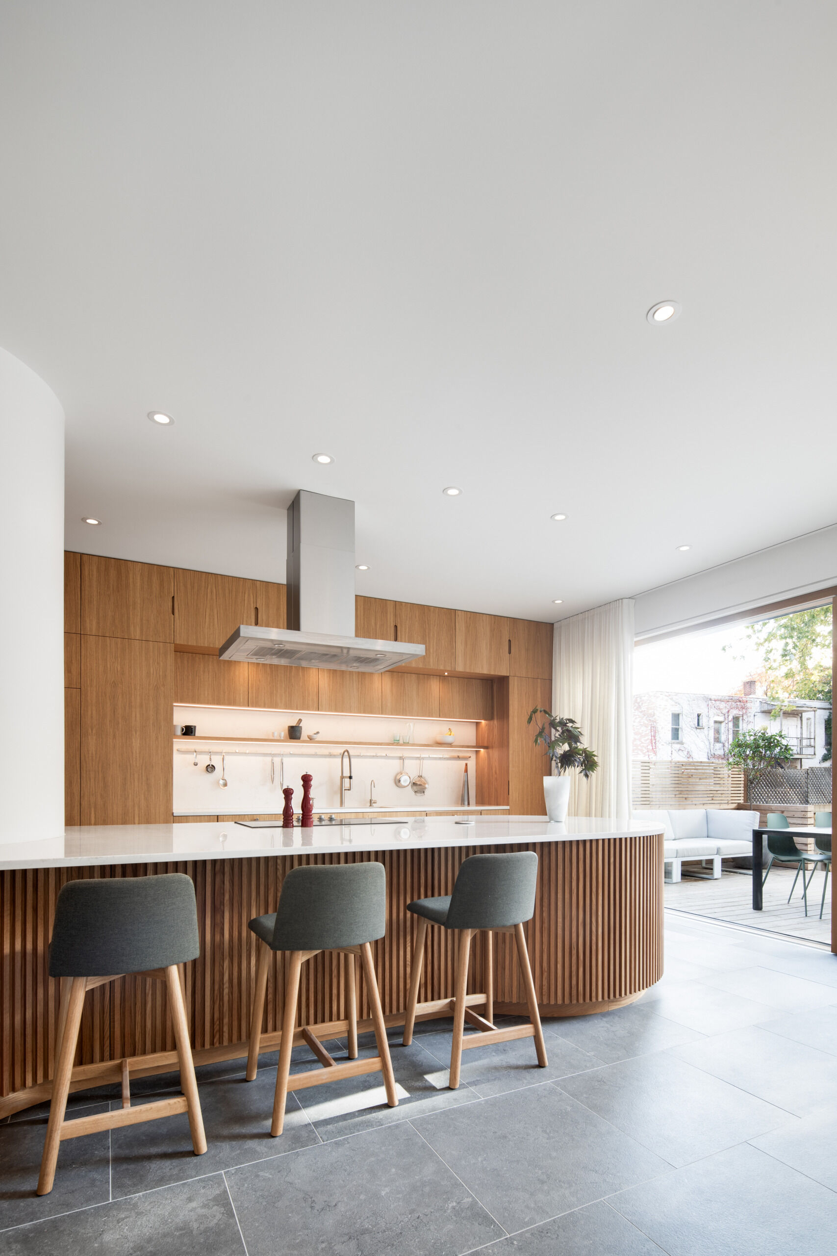 A sculptural oak island and seamless floor-to-ceiling cabinetry define this light-filled Montreal kitchen, where natural materials and soft curves create a warm, minimalist atmosphere.