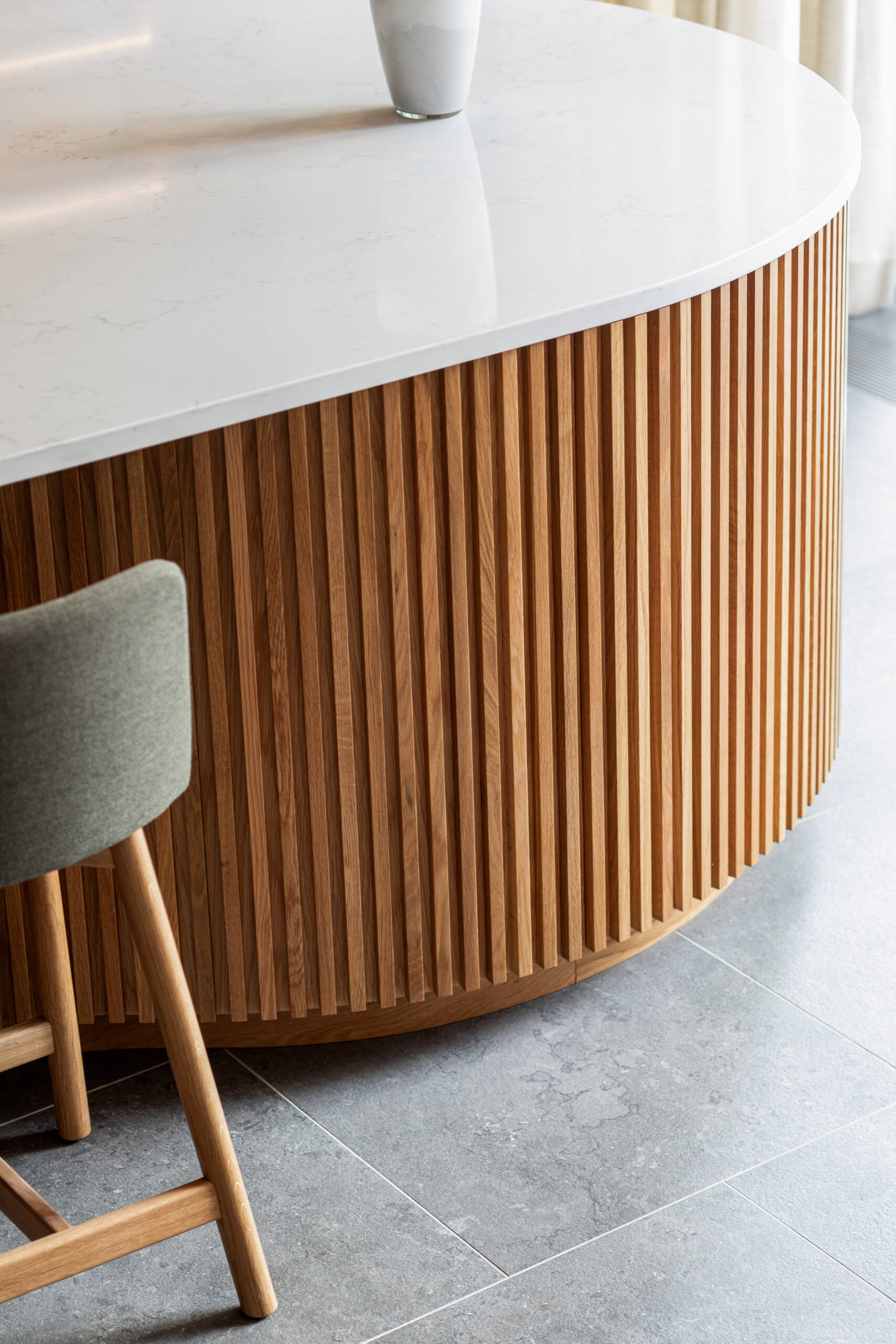 A sculptural oak island and seamless floor-to-ceiling cabinetry define this light-filled Montreal kitchen, where natural materials and soft curves create a warm, minimalist atmosphere.
