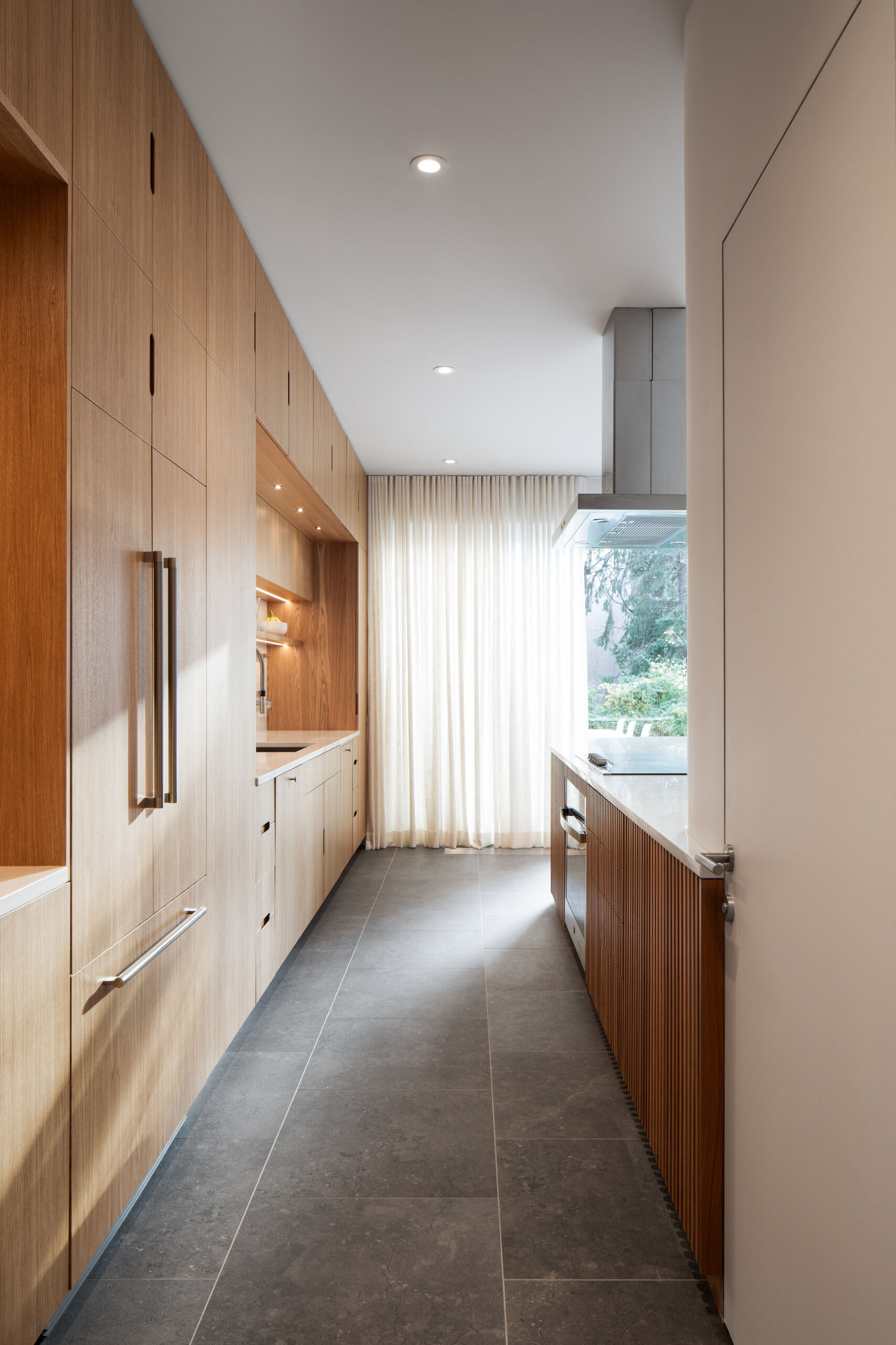 A sculptural oak island and seamless floor-to-ceiling cabinetry define this light-filled Montreal kitchen, where natural materials and soft curves create a warm, minimalist atmosphere.