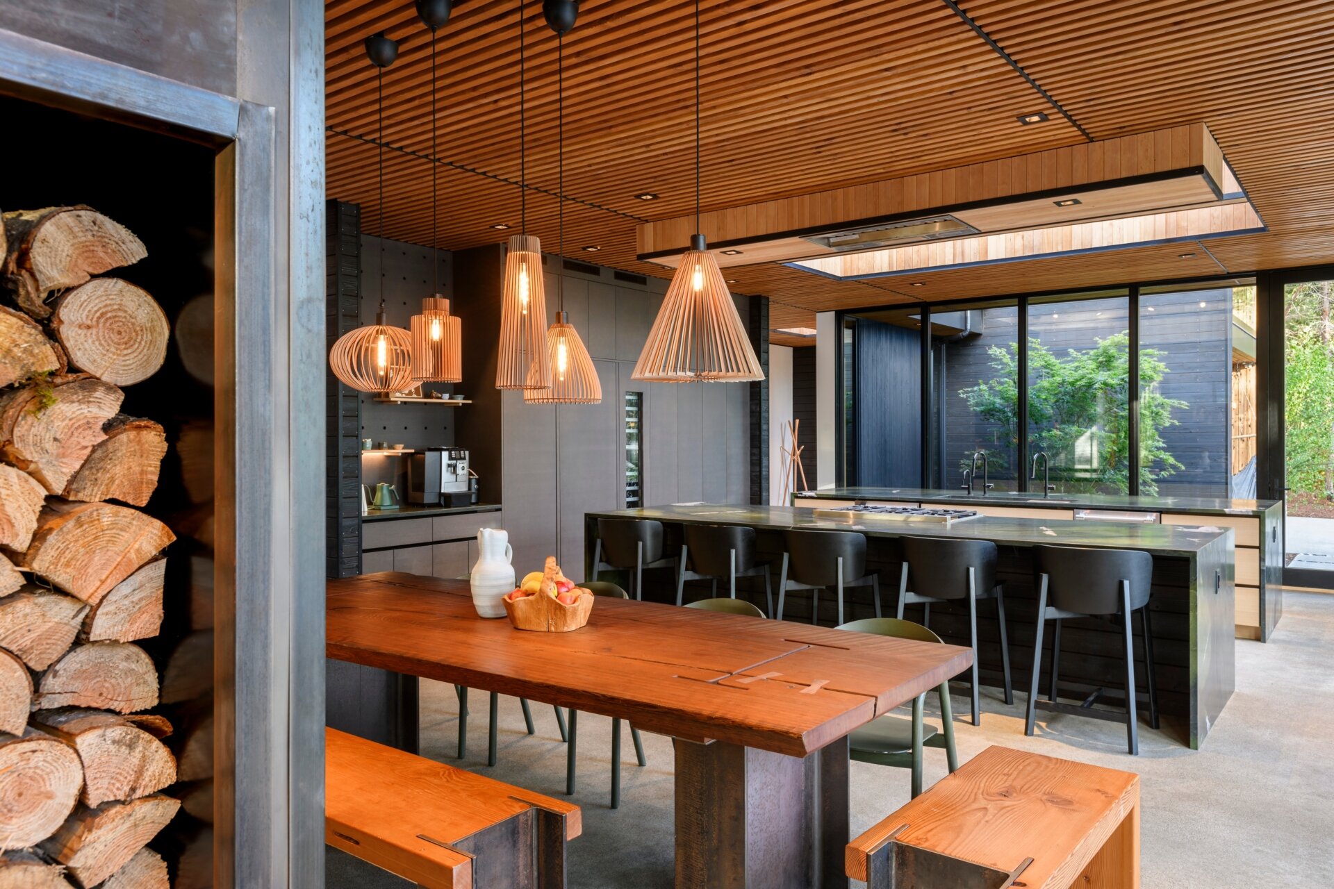 A warm, modern dining space with concrete floors, sculptural lighting, and floor-to-ceiling forest views, perfect for slow meals and quiet moments.