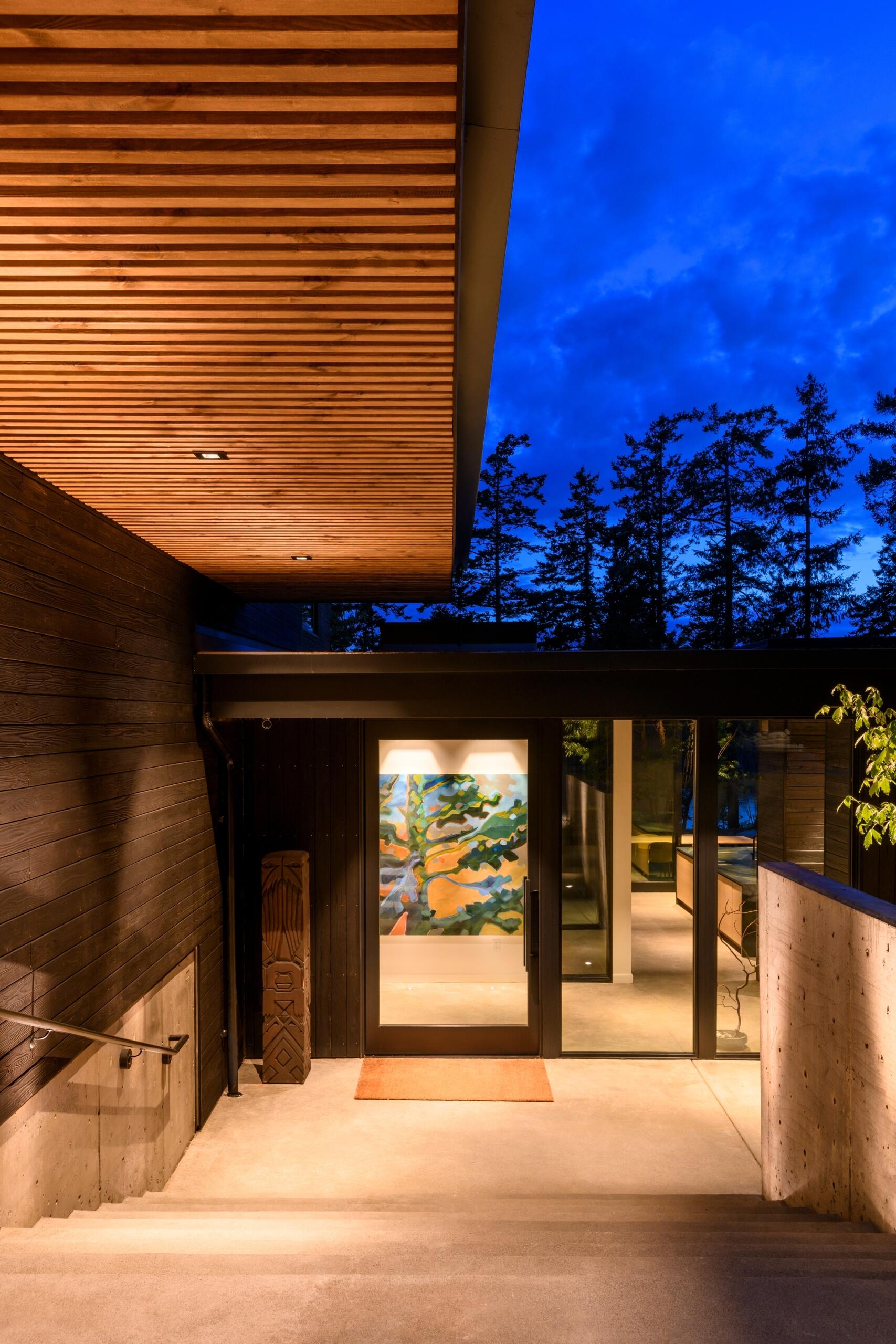 The home is accessible from both a driveway and a footpath, reflecting the dual modes of arrival common to the island. The entry sequence is subtle, with minimal hardscape and native landscaping that blends into the forested site.