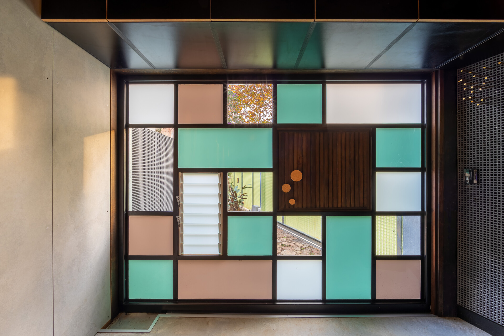 At street level, the garage door brings playful personality to a practical space with its mosaic of frosted, aqua, and blush-toned glass panels. The geometric design feels fresh and creative, letting soft natural light filter through while still offering privacy.