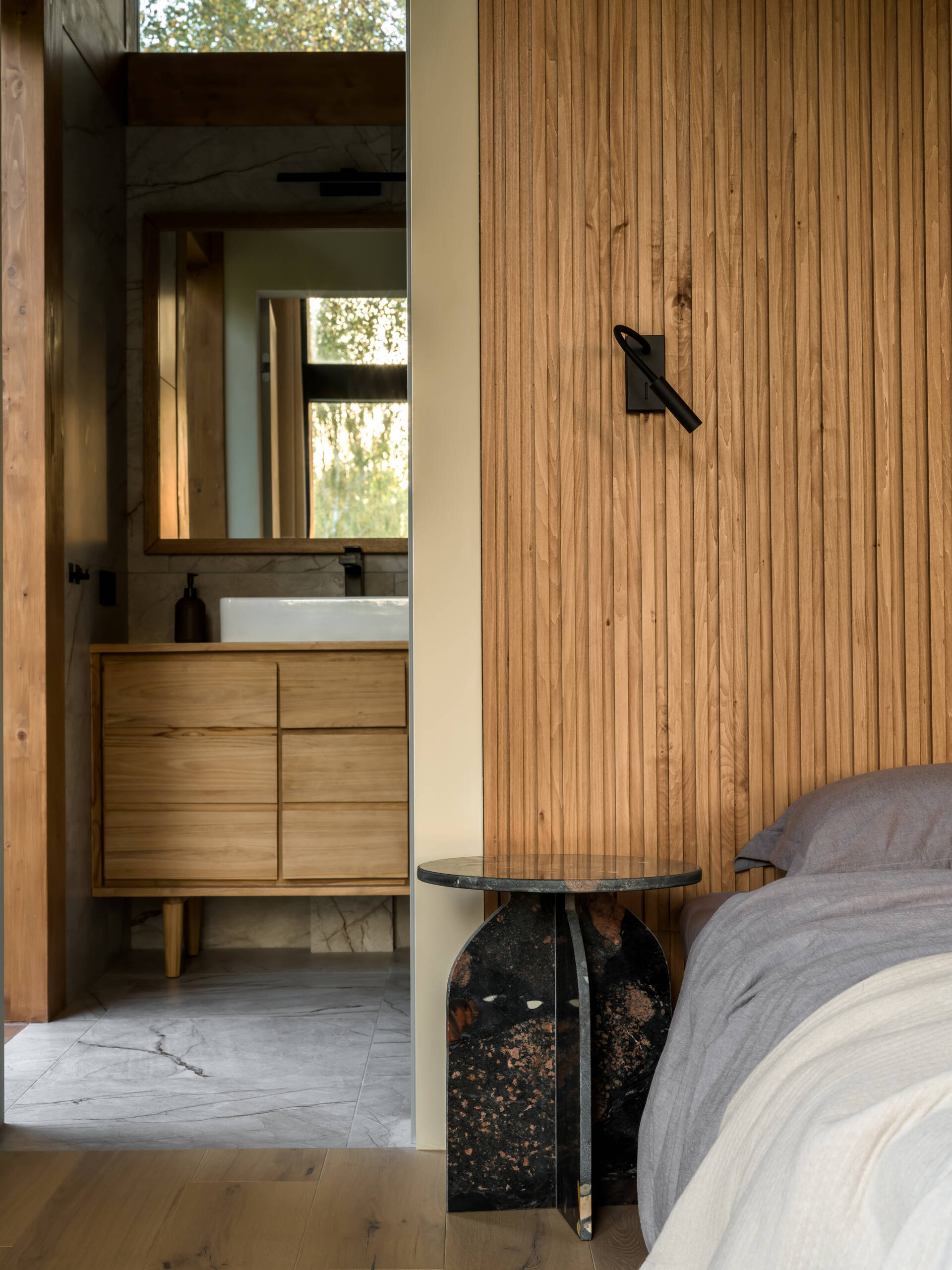 Textured stone, ribbed wood, and clean-lined furniture define this light-filled bedroom with panoramic views and a calming material palette.