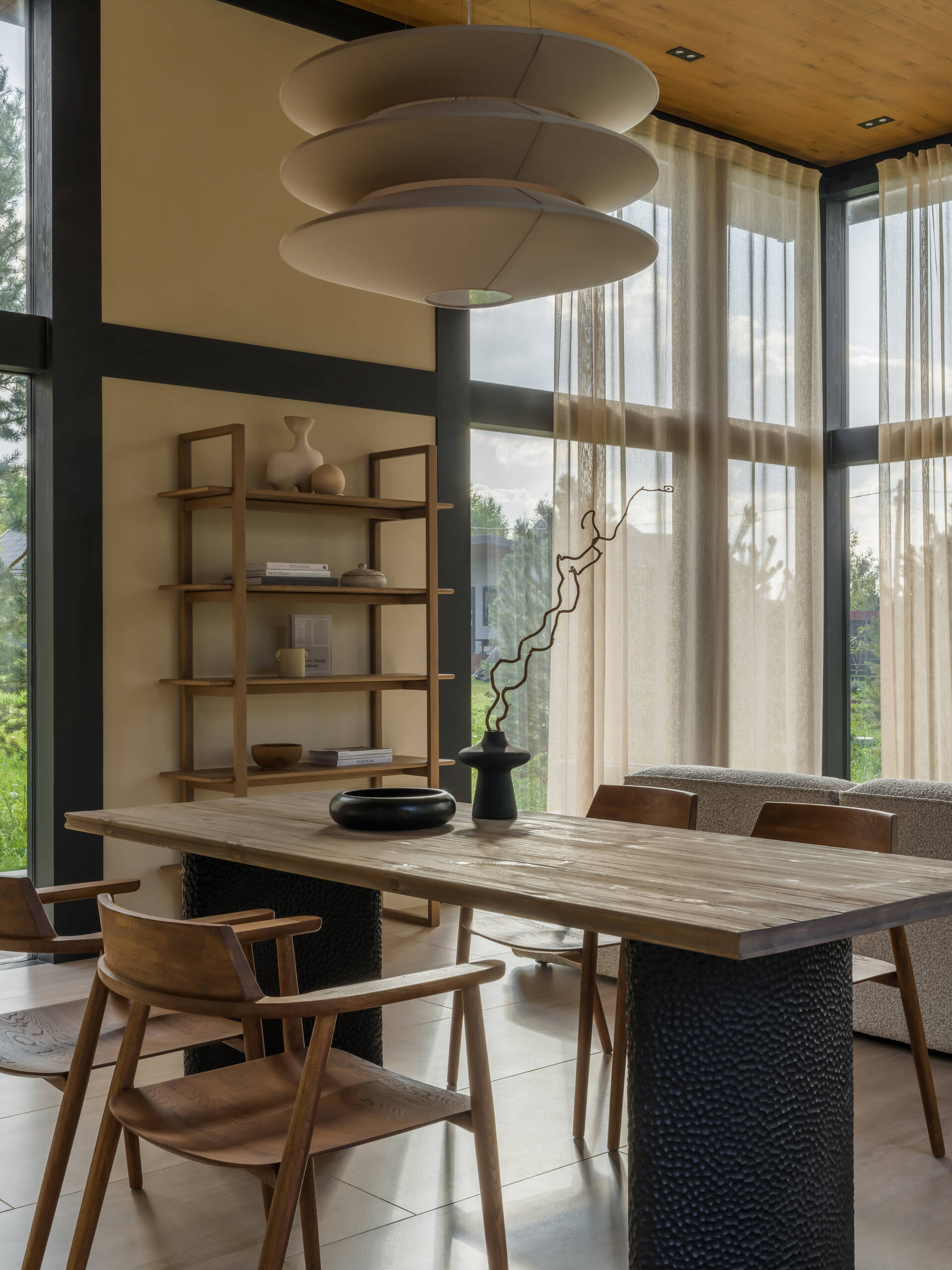 Warm wood and stone textures define this dining area, where a Volcano table and minimalist chairs sit under a soft, sculptural pendant light.