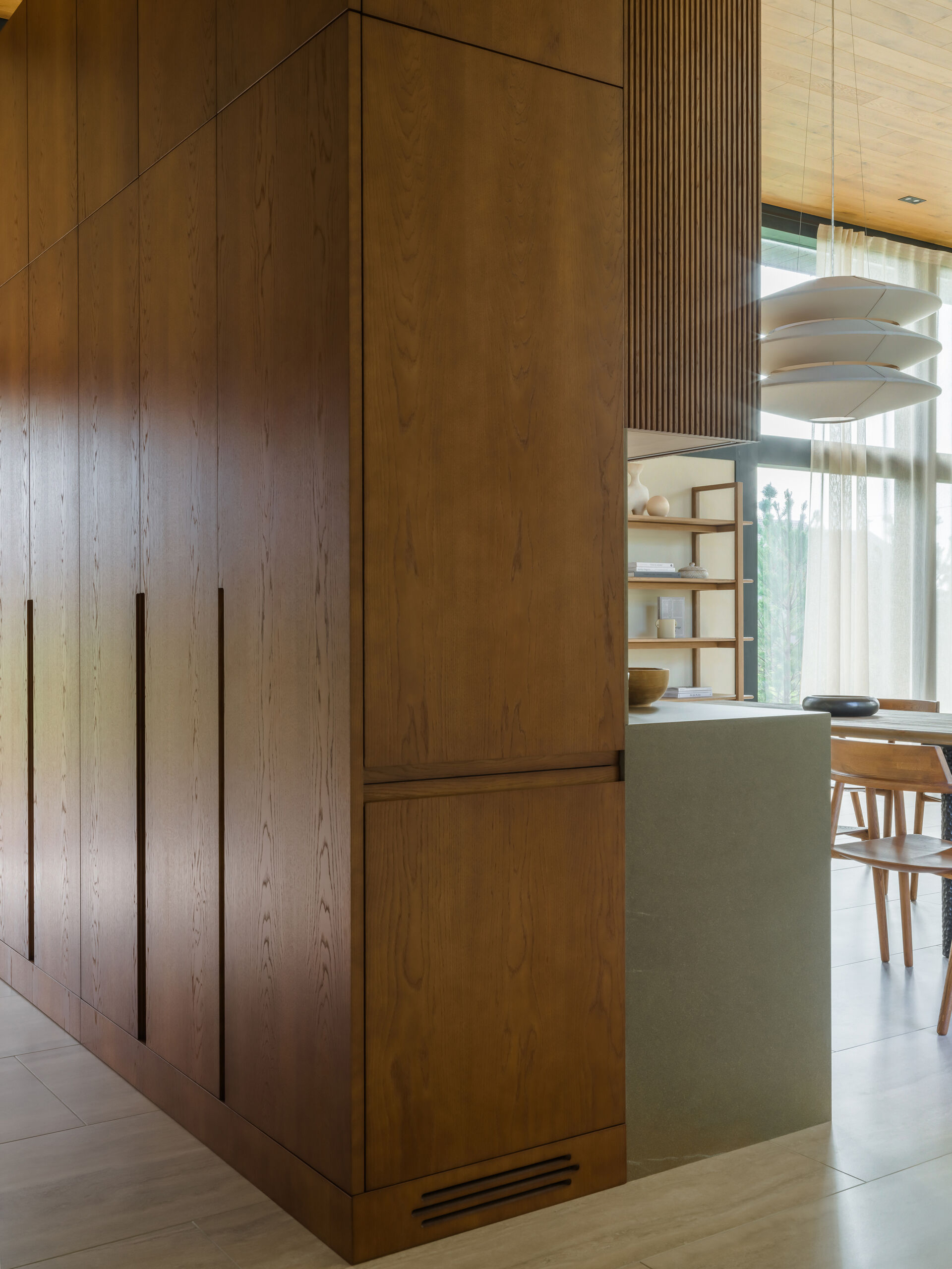 A sculptural, amber-toned kitchen unit by Dantone Home anchors the layout, blending beauty and function with warm wood textures and smart storage.