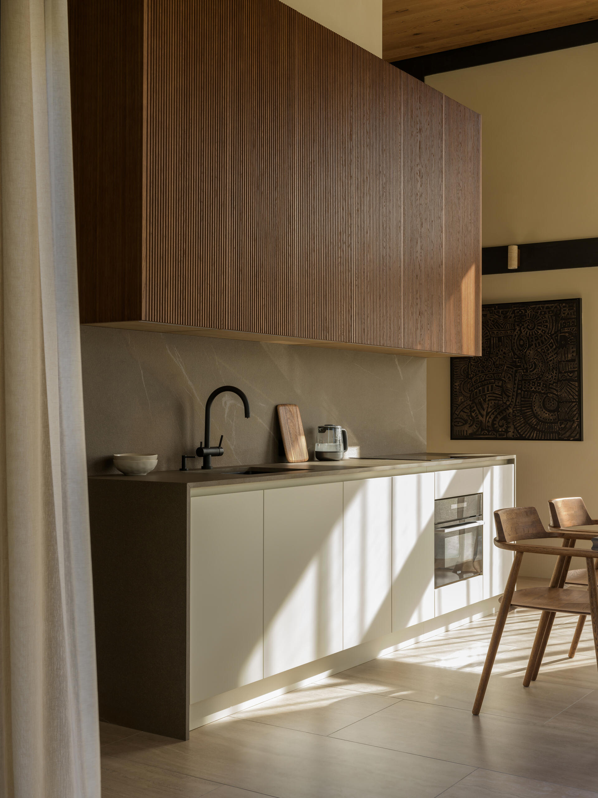 A sculptural, amber-toned kitchen unit by Dantone Home anchors the layout, blending beauty and function with warm wood textures and smart storage.
