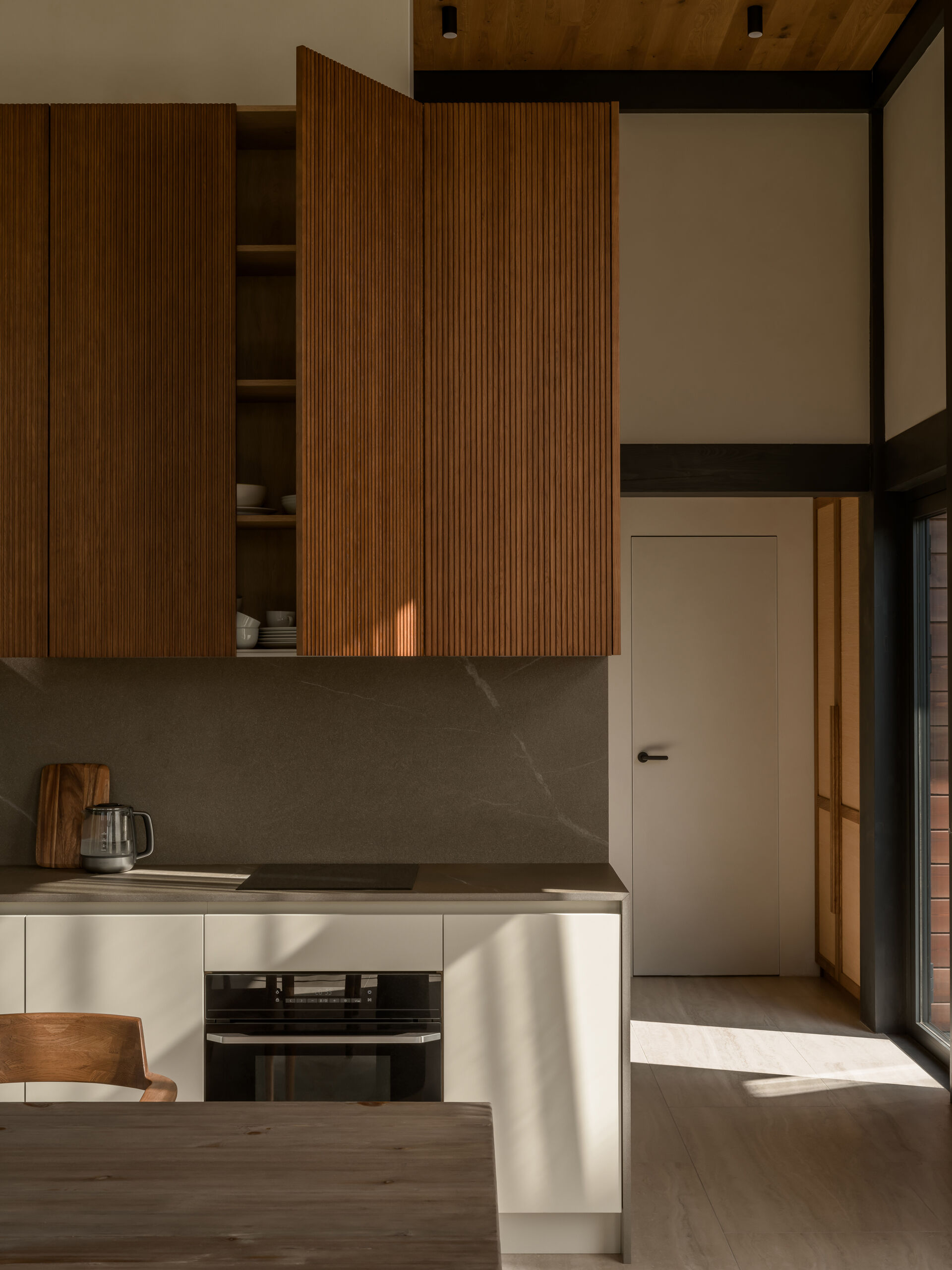 A sculptural, amber-toned kitchen unit by Dantone Home anchors the layout, blending beauty and function with warm wood textures and smart storage.