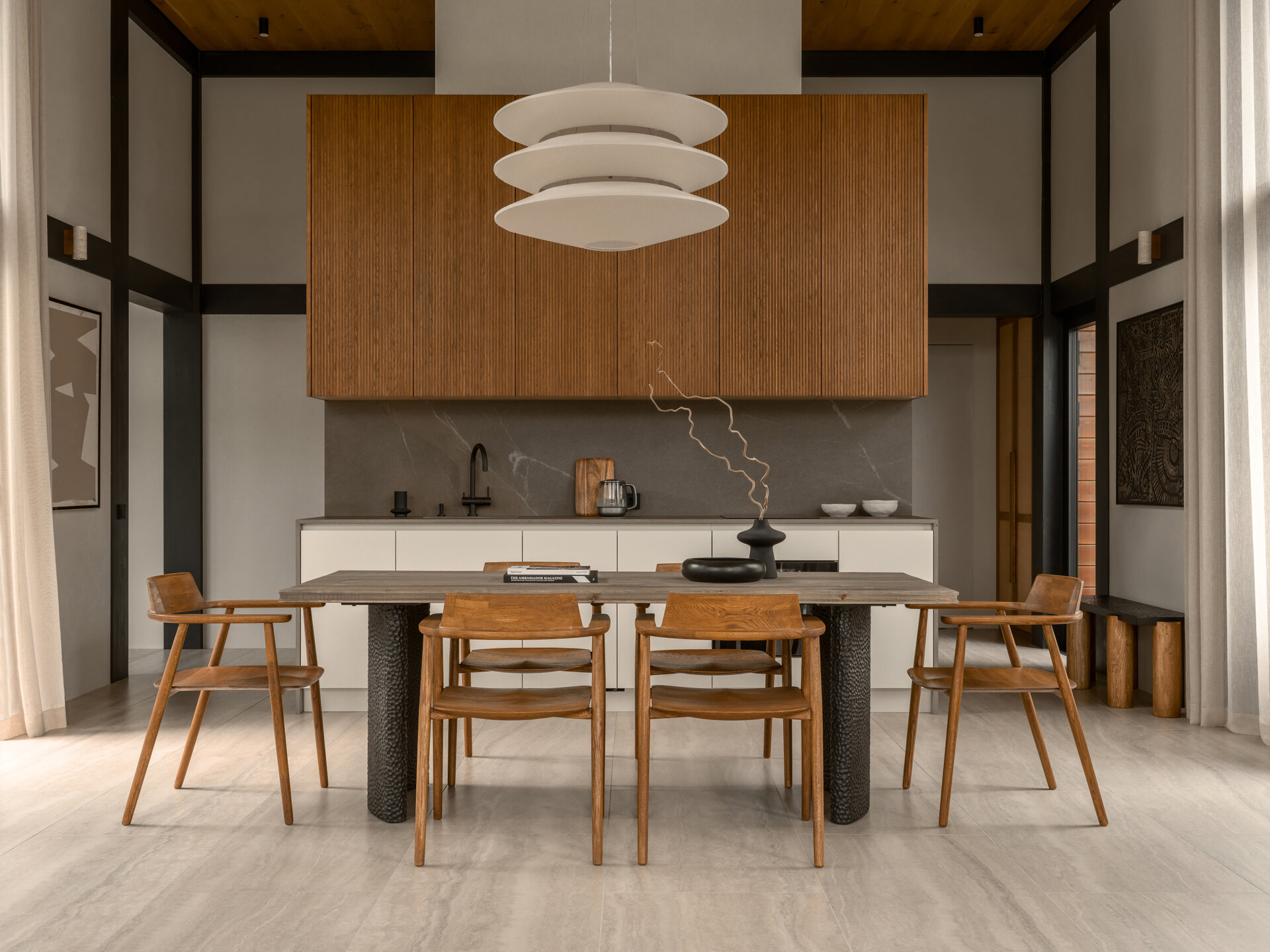 Warm wood and stone textures define this dining area, where a Volcano table and minimalist chairs sit under a soft, sculptural pendant light.