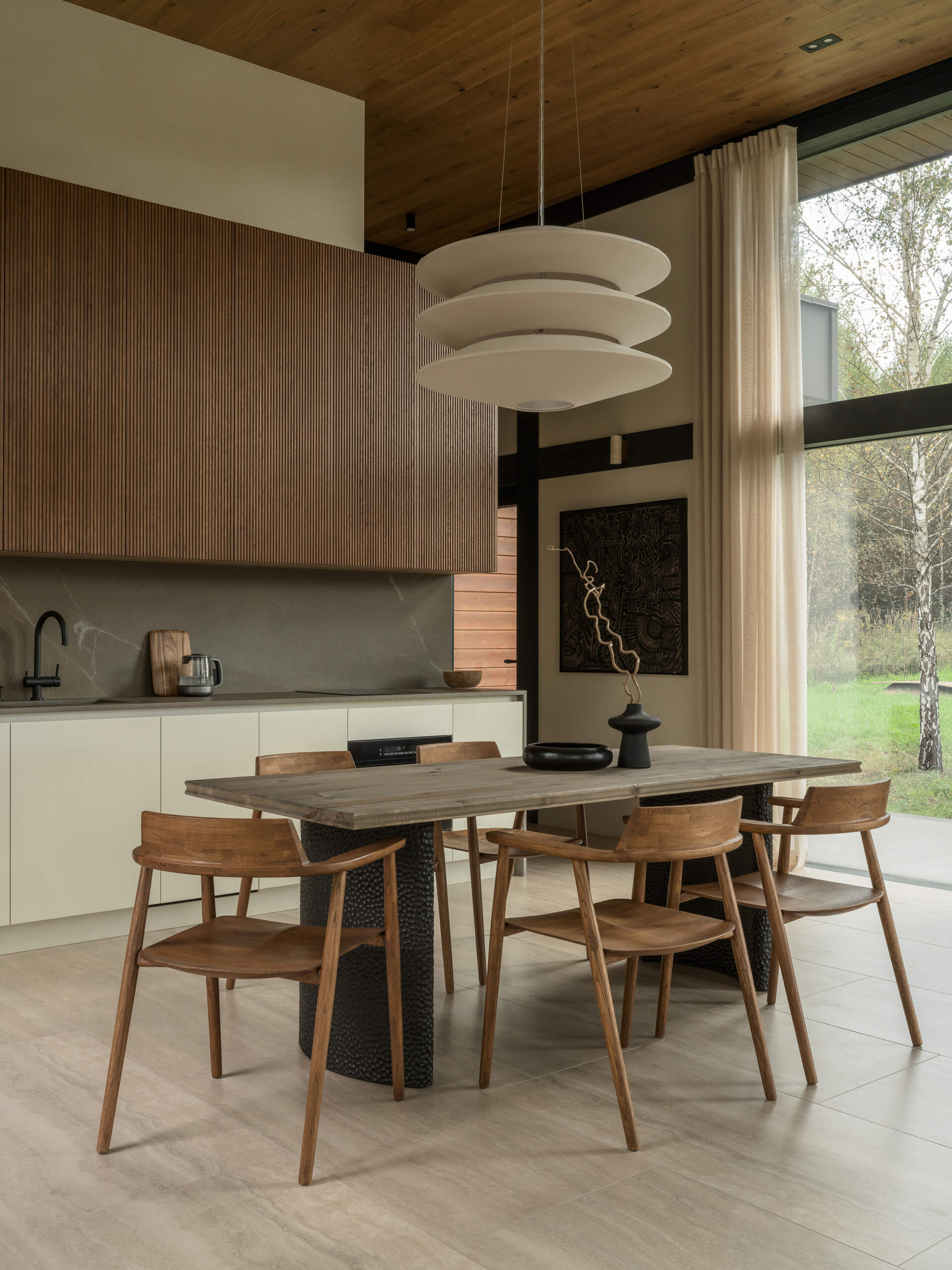 Warm wood and stone textures define this dining area, where a Volcano table and minimalist chairs sit under a soft, sculptural pendant light.
