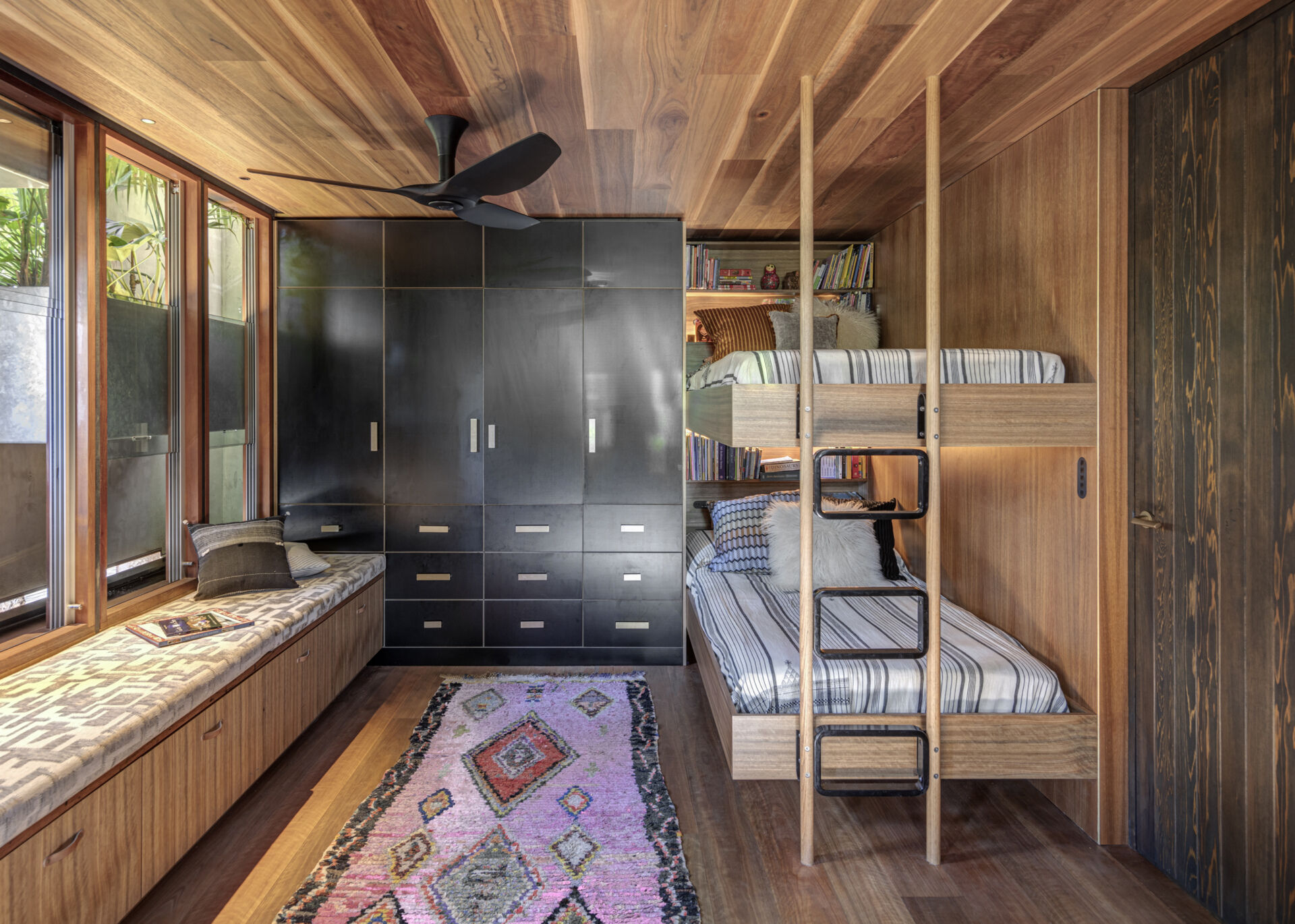 The kids’ room balances warmth and utility with built-in bunk beds, and cabinetry that keeps the space tidy. A long window seat offers a quiet spot to read, while soft rugs and low tables encourage play and creativity in a calm, light-filled setting.