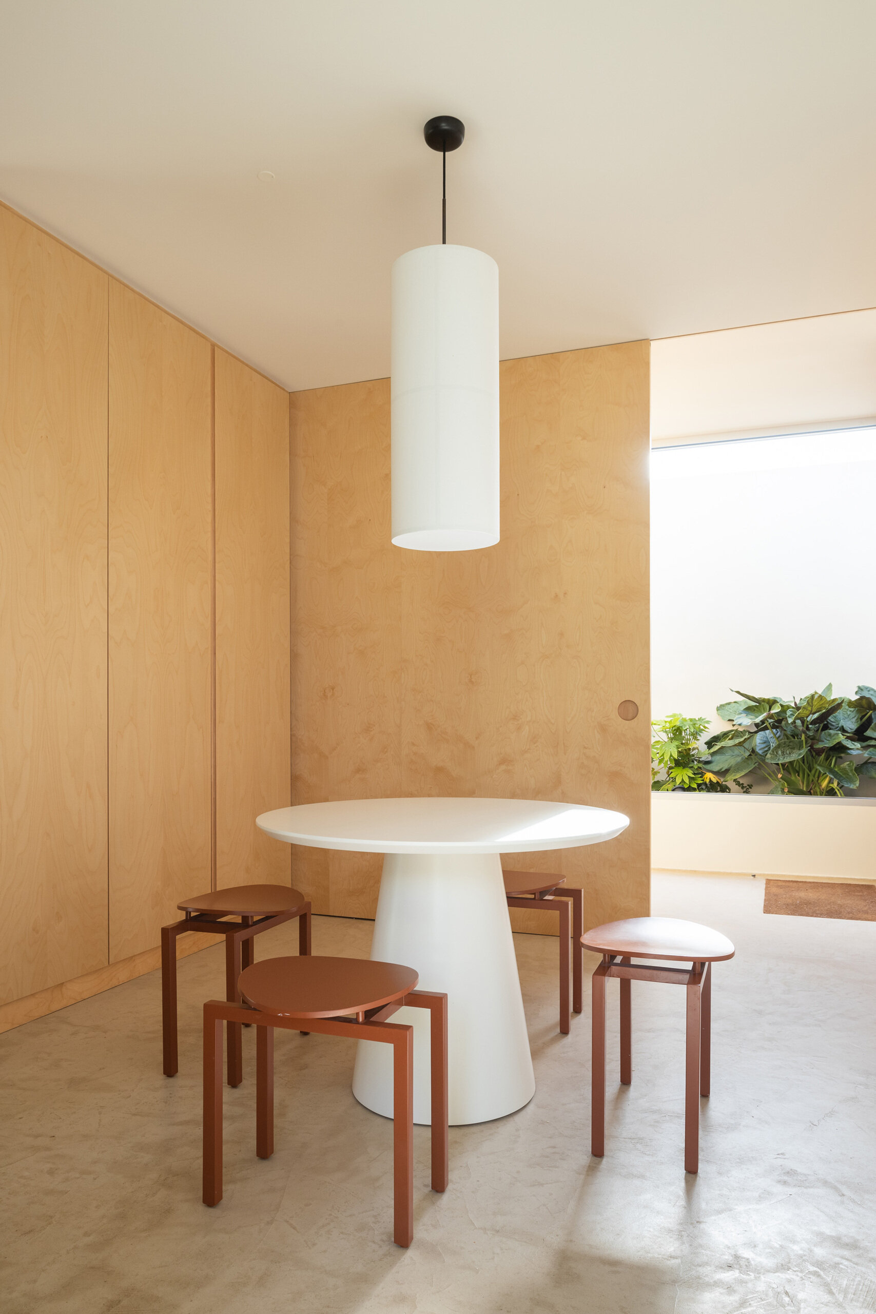 The kitchen continues the palette of quiet, natural materials, where a dining nook feels both modern and warm, with rust-colored stools and a sculptural white table set against pale wood cabinetry.