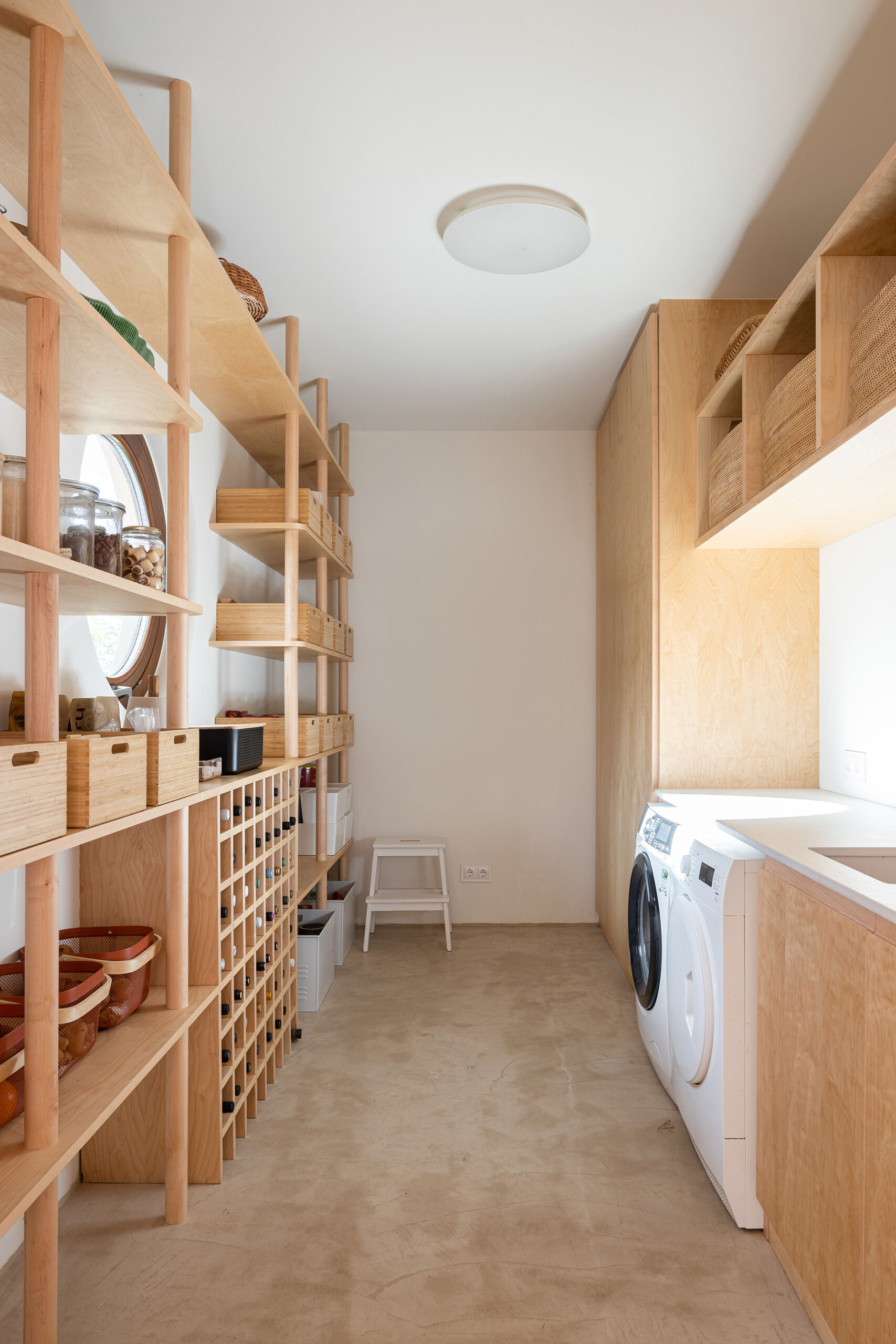 Close by to the kitchen, a light-filled laundry and pantry room feels beautifully organized, with wood shelves and cabinets that keep everything calm and tidy. Thoughtful baskets and glass jars line the open storage, adding a touch of rustic charm while staying practical.