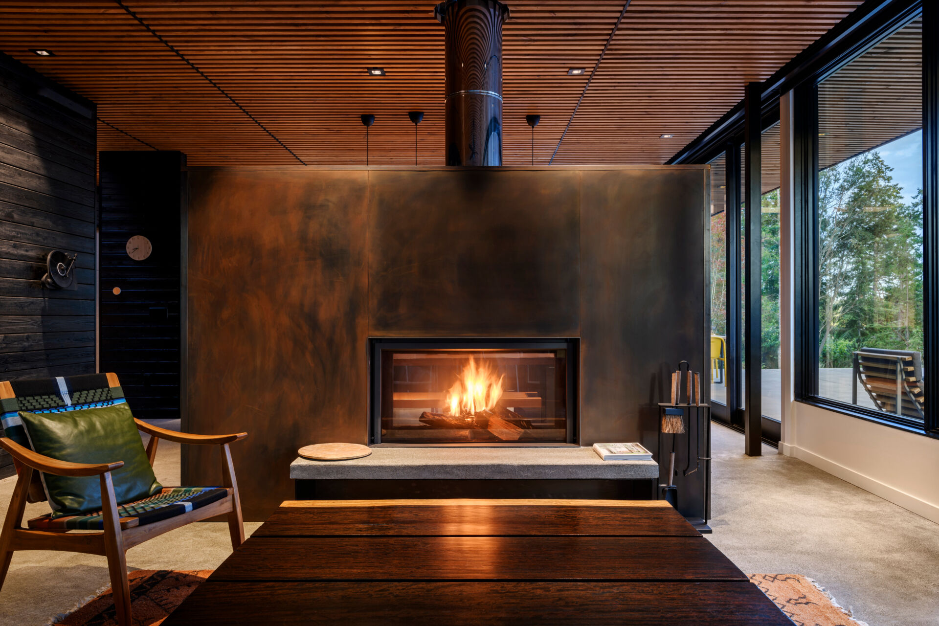 Large windows and a corten steel fireplace anchor this open, light-filled living space with views to the water.