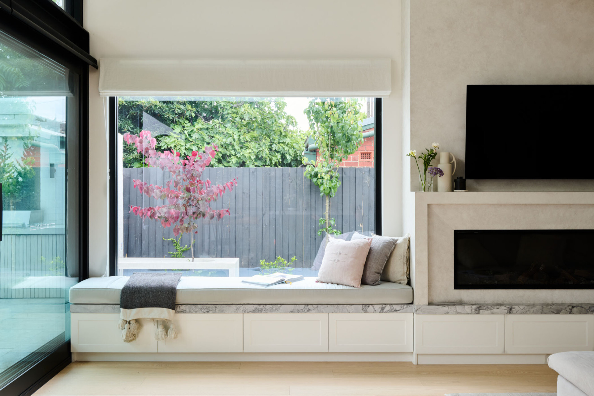 A built-in window bench, elegant fireplace, and framed garden views turn this living room into a cozy, light-filled escape designed for both comfort and calm.