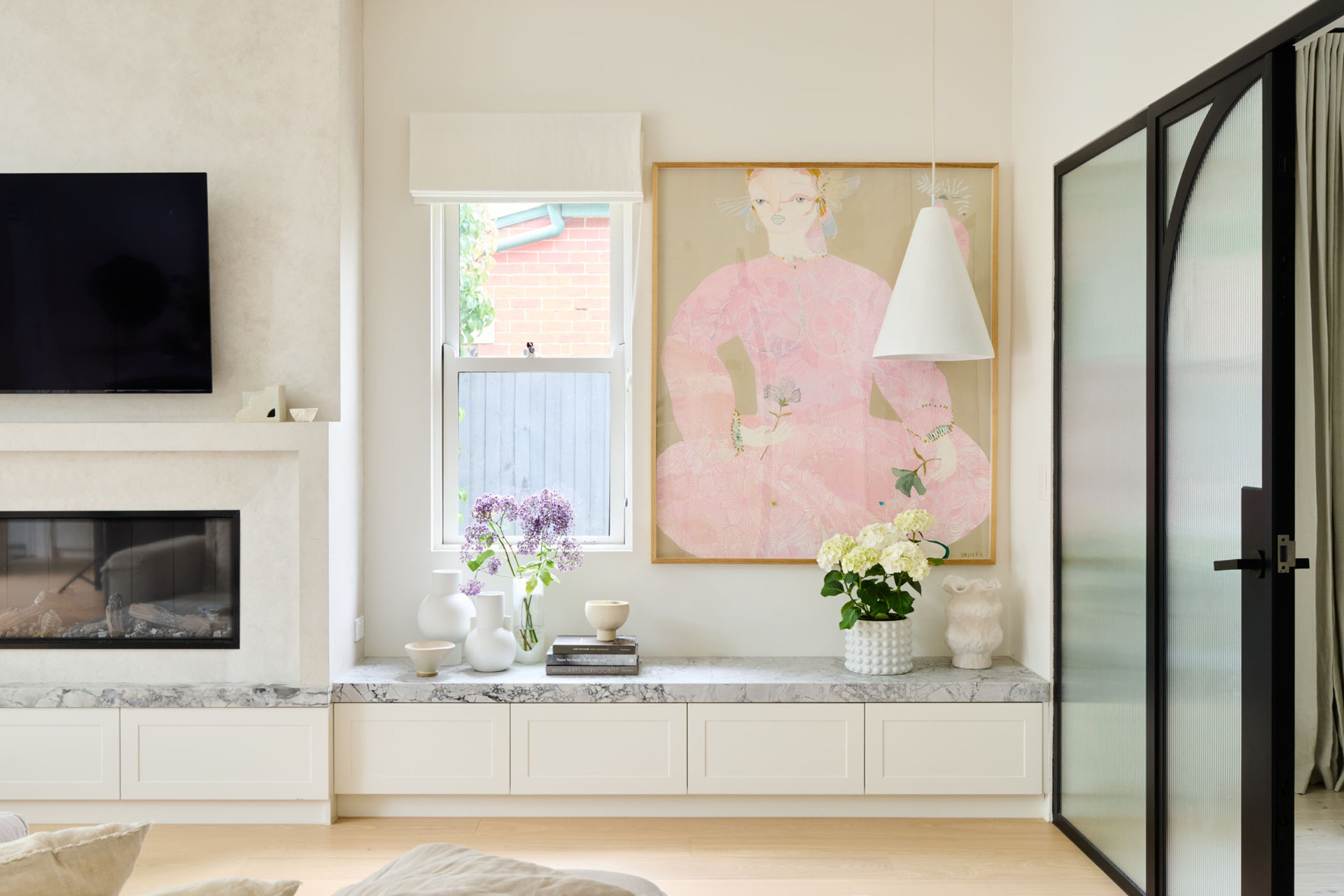 A built-in shelf and storage, elegant fireplace, and framed garden views turn this living room into a cozy, light-filled escape designed for both comfort and calm.