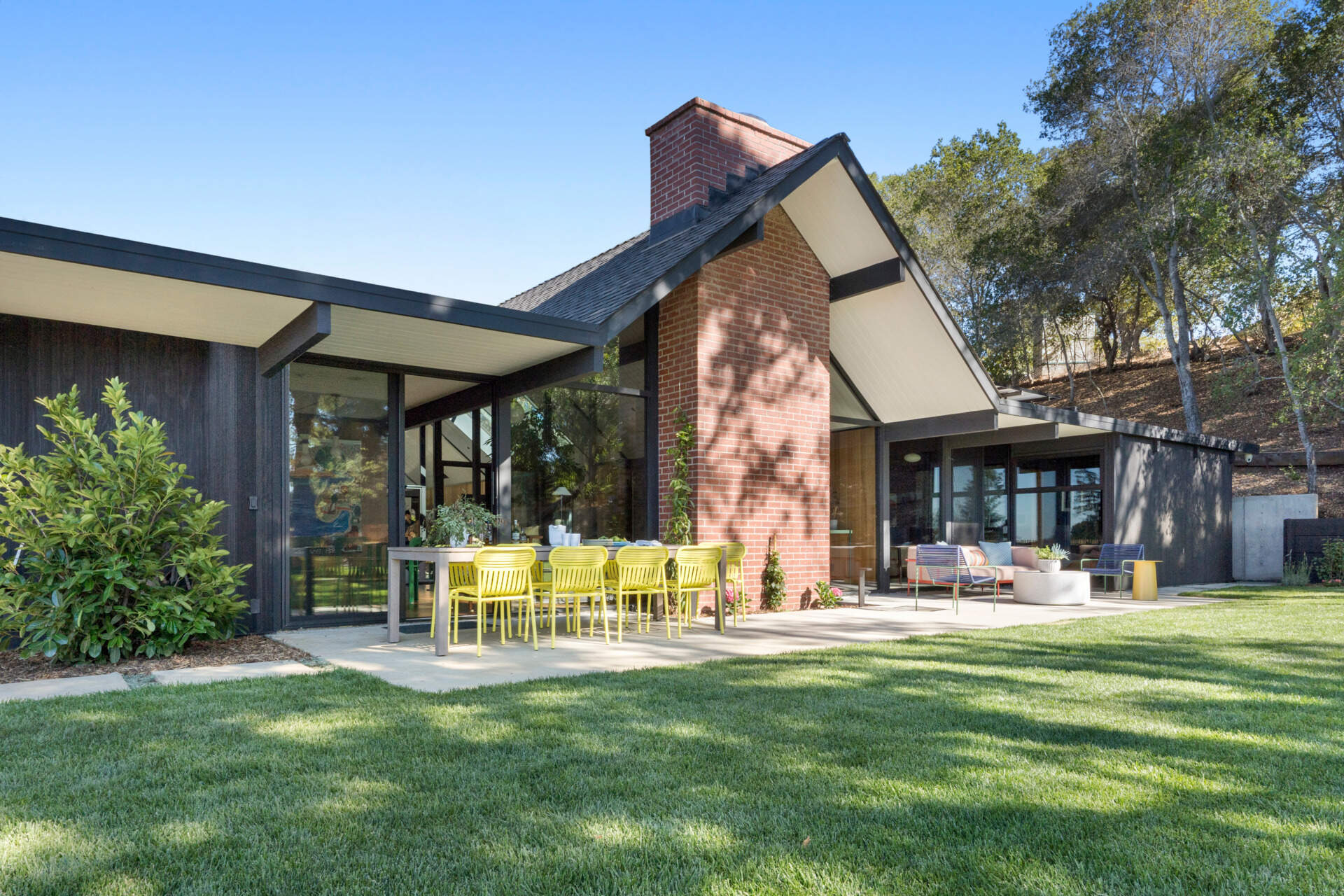 Set back from the street and accessed via a long driveway, the residence combines privacy with striking form. Its exterior has been updated using Shou Sugi Ban Accoya barn wood siding, adding texture and durability. A central gabled roof defines the structure, flanked by two flat-roofed wings that retain the home's mid-century profile.