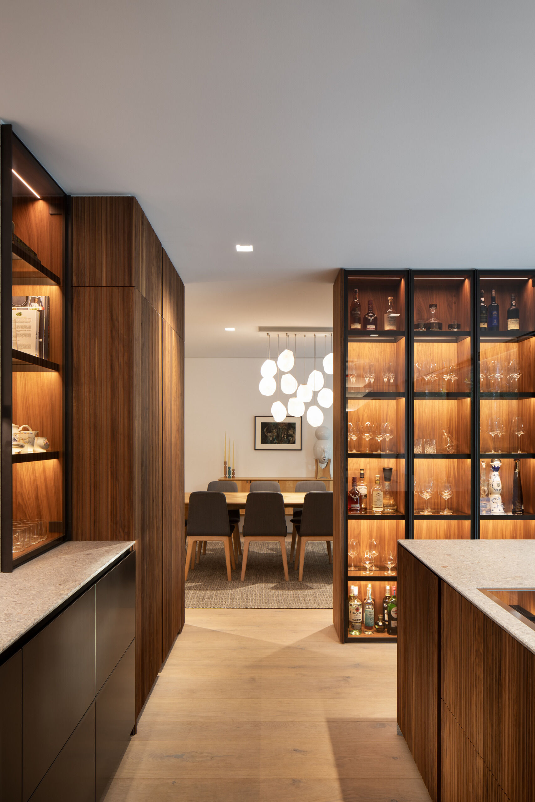 The dining area, framed by rich wood cabinetry in the kitchen, has soft neutrals and sculptural pendant lights that create a calm, inviting space for good food and easy conversation.