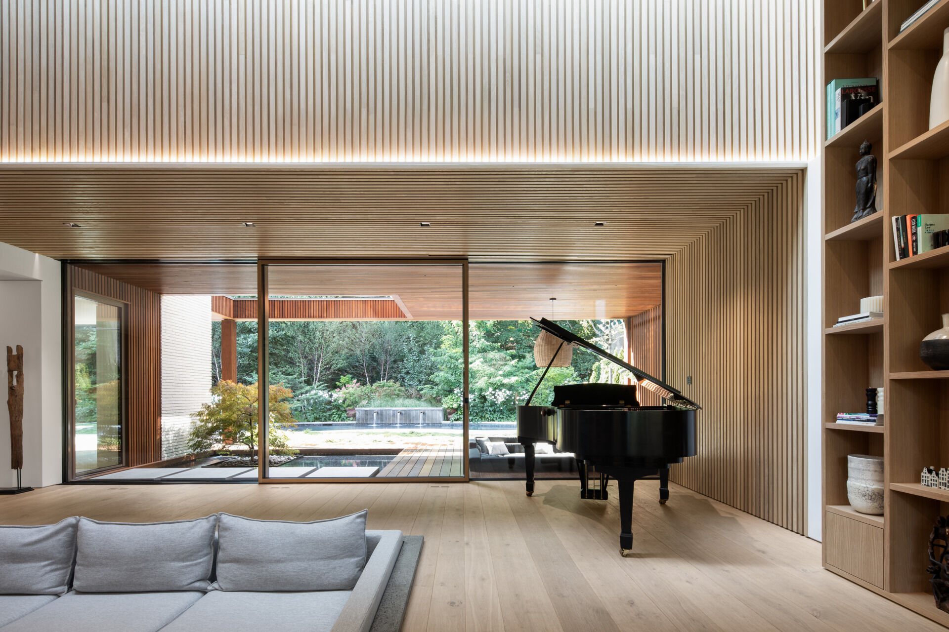 Inside, the living area is a lesson in restraint. Natural oak and walnut meet stone and marble, with no baseboards or moldings in sight. The double-height cathedral ceiling brings a sense of drama, softened by curves and textured surfaces. Hidden doors and architectural lighting preserve the visual flow, letting materiality and form do the talking.