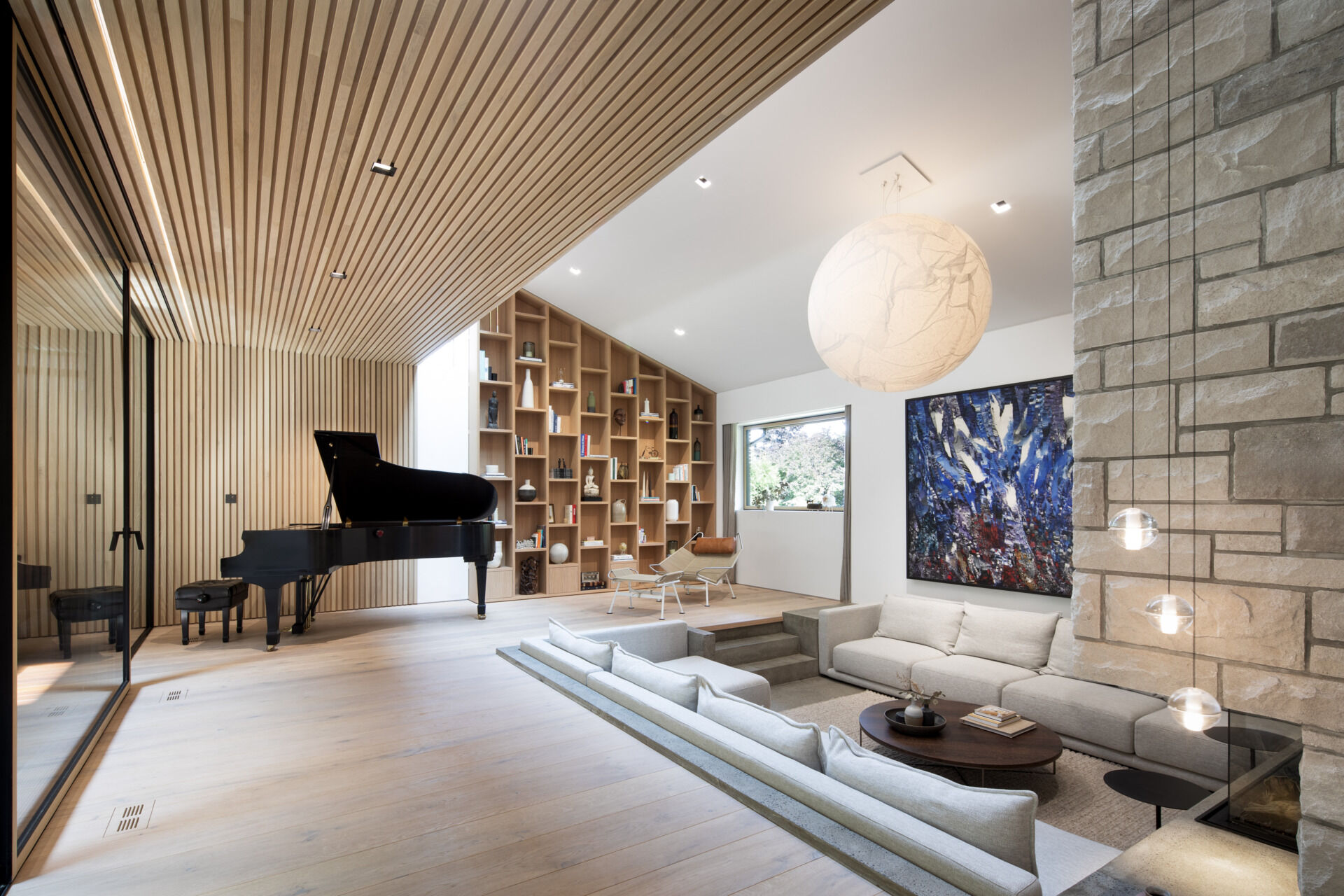 Inside, the living area is a lesson in restraint. Natural oak and walnut meet stone and marble, with no baseboards or moldings in sight. The double-height cathedral ceiling brings a sense of drama, softened by curves and textured surfaces. Hidden doors and architectural lighting preserve the visual flow, letting materiality and form do the talking.